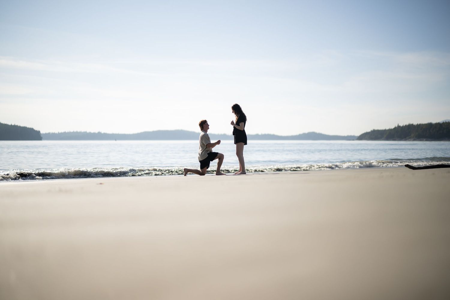 Wide angle view of a scenic beach with distant mountains and people walking on the sand.