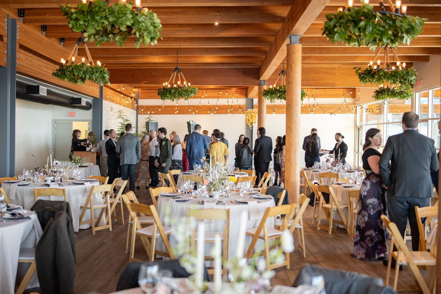 Elegant reception venue with wooden beams, hanging plants and round tables set for dining.