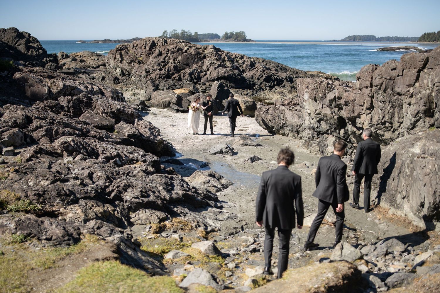 Wedding party walking along scenic coastal path with rocky cliffs and ocean views.