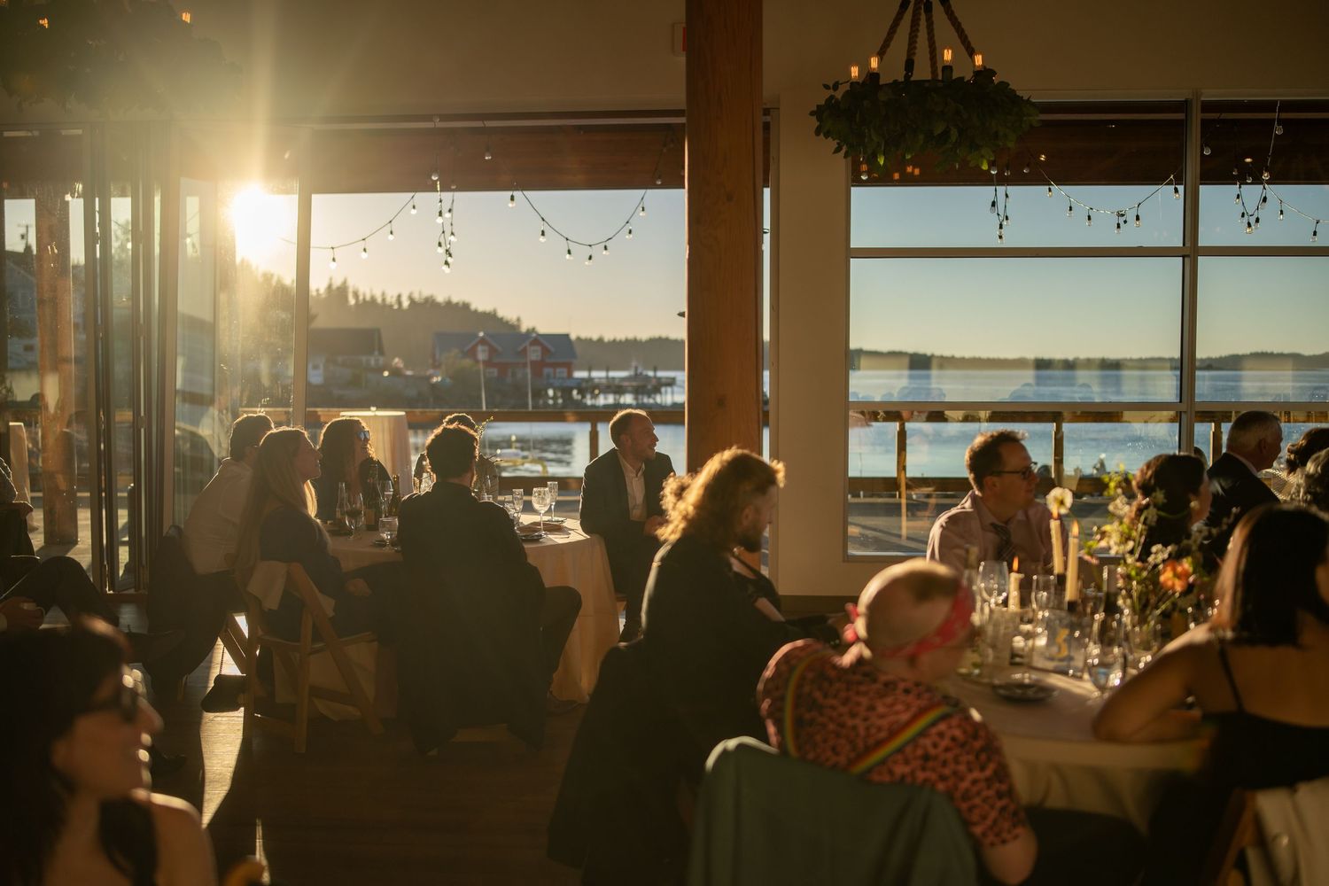 Sunset light streams through windows of an elegant waterfront venue during a wedding reception.