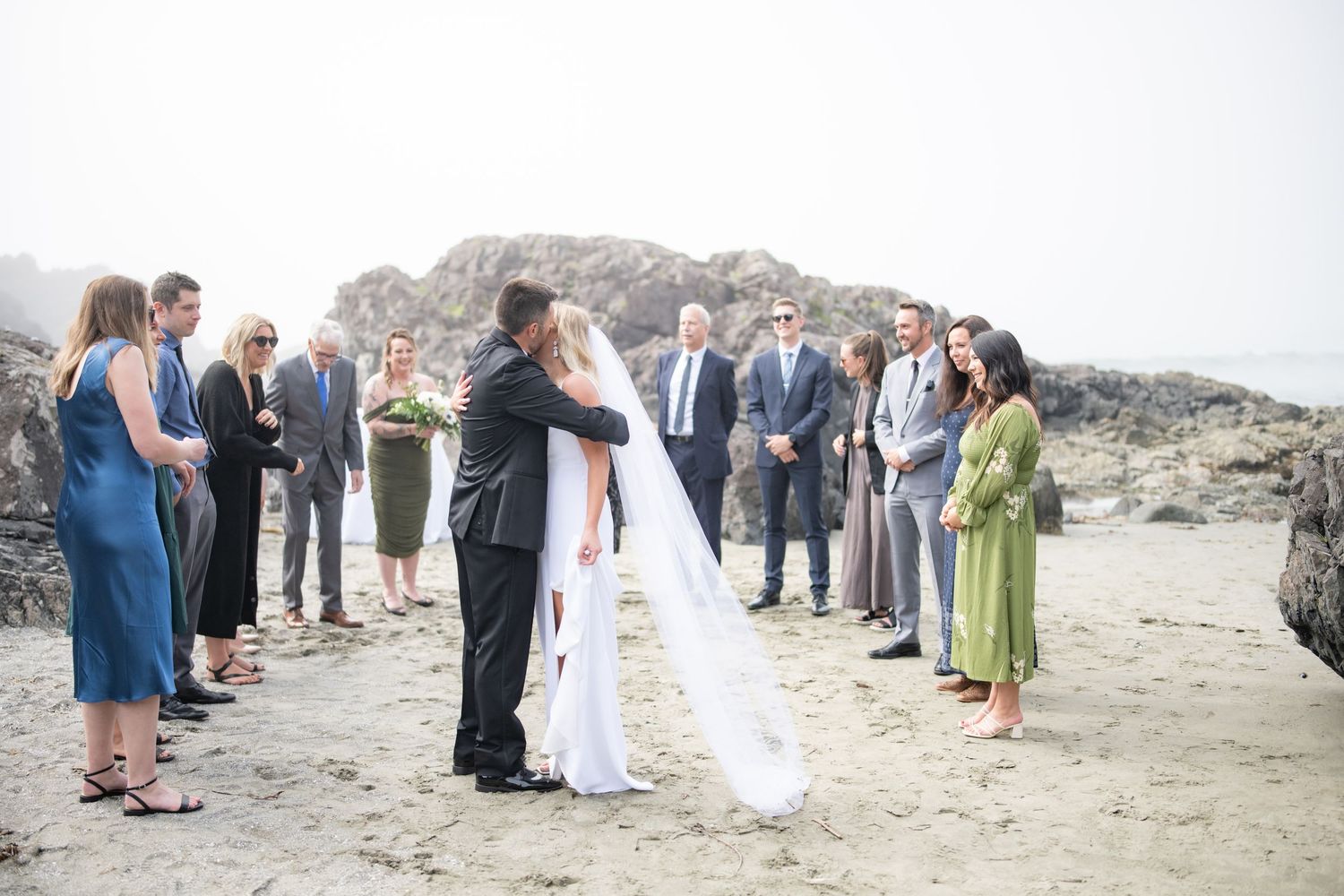 Wedding party lined up along rocky coastal cliffs during outdoor ceremony.