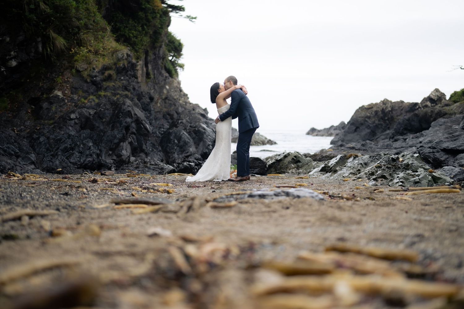 Wedding couple stands on rugged coastline with dramatic cliffs and ocean views.