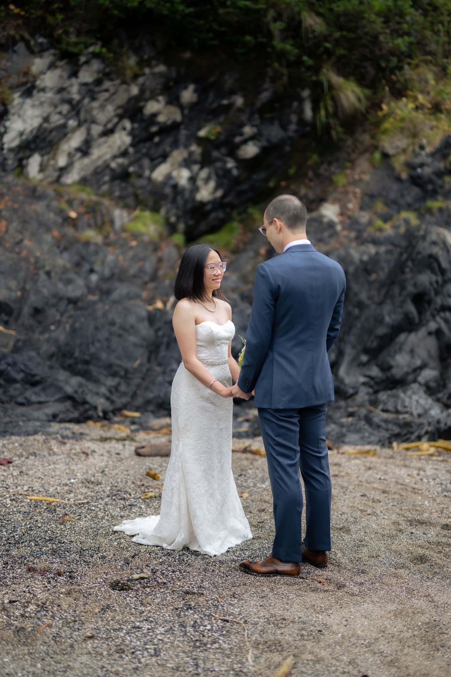 Wedding couple shares a special moment on a rocky beach with dramatic coastal cliffs.