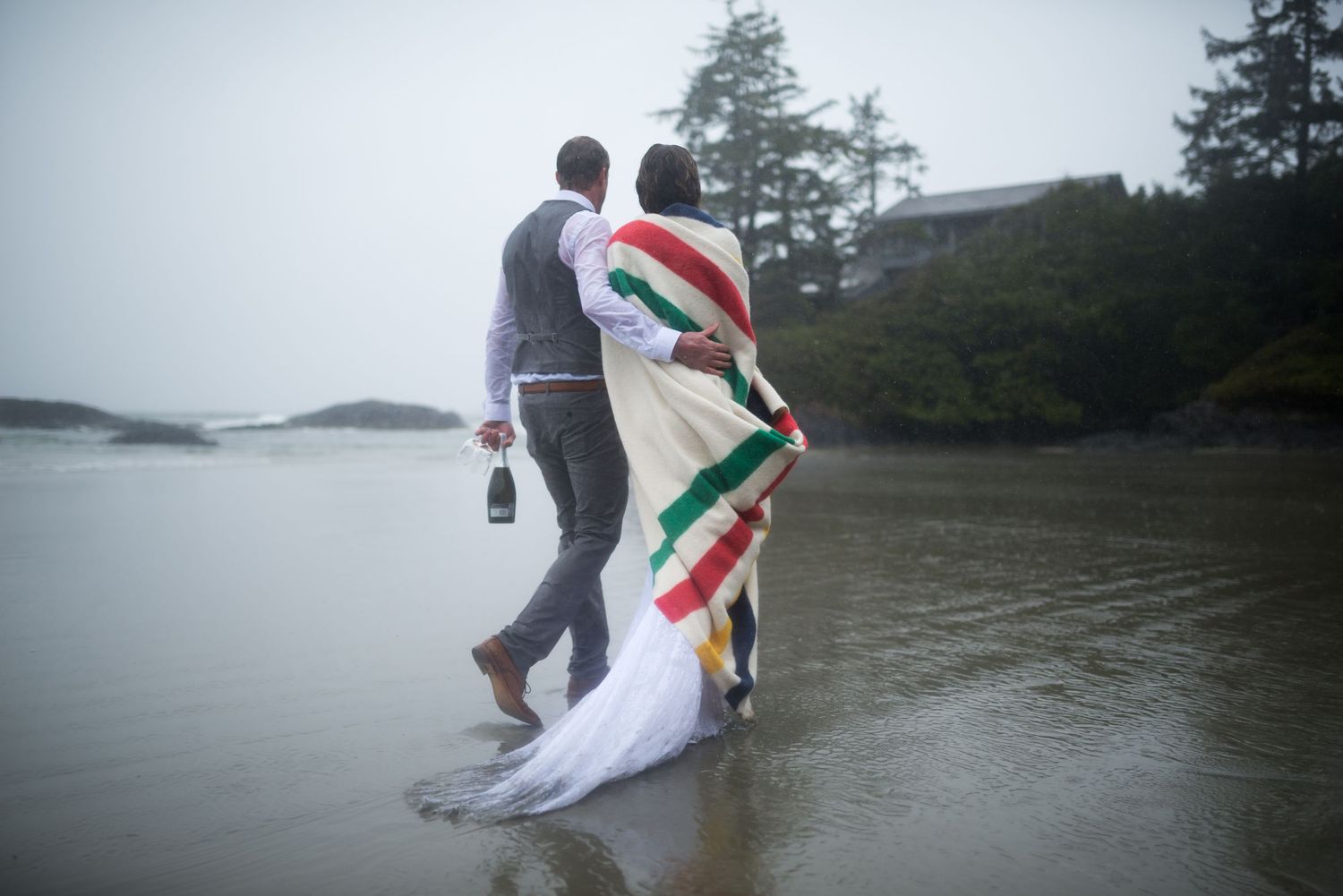 Couple walking near water's edge with a colorful striped blanket.
