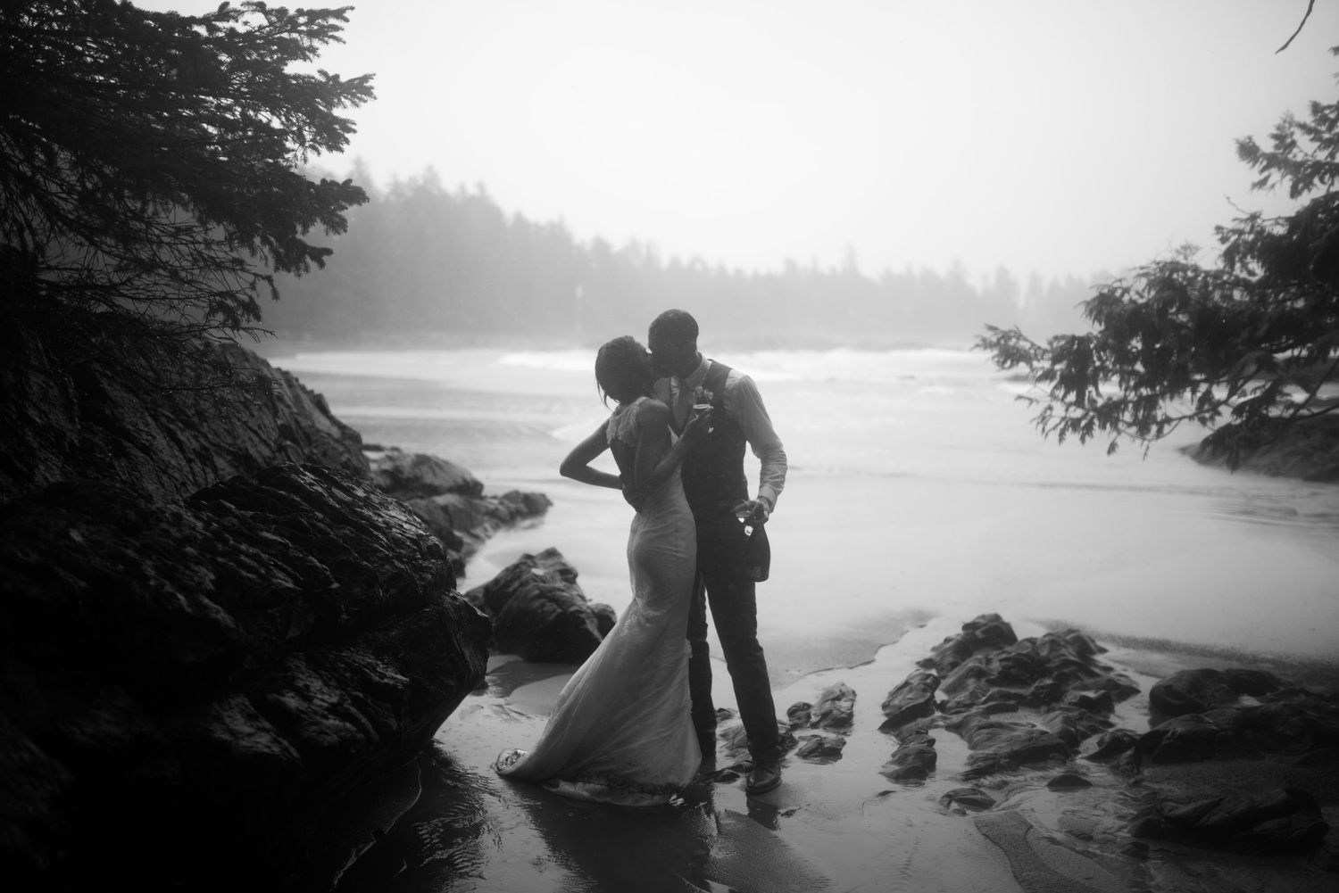Silhouetted figures on rocky beach during misty sunset.