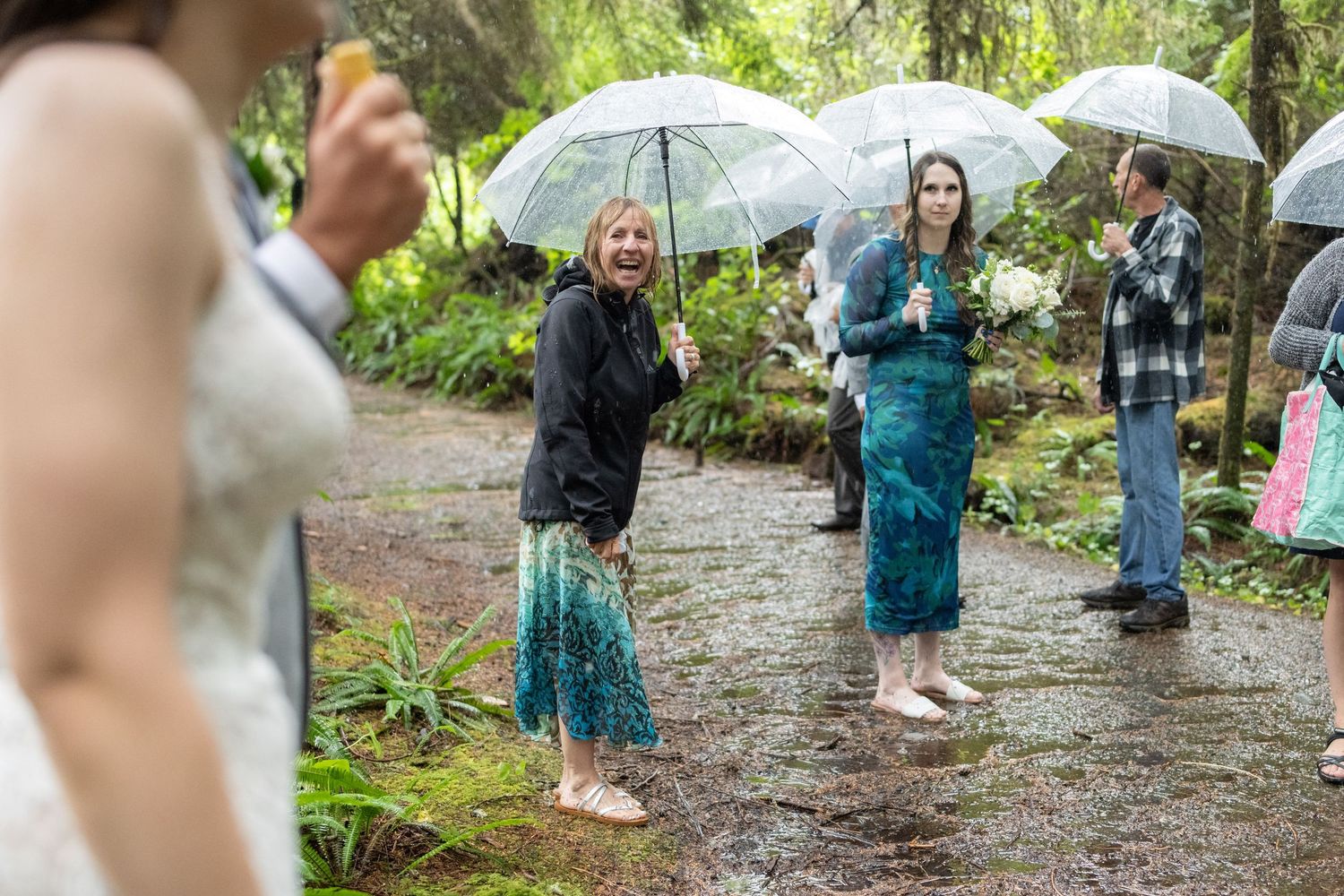 Group gathering on a forest path with umbrellas during light rain.