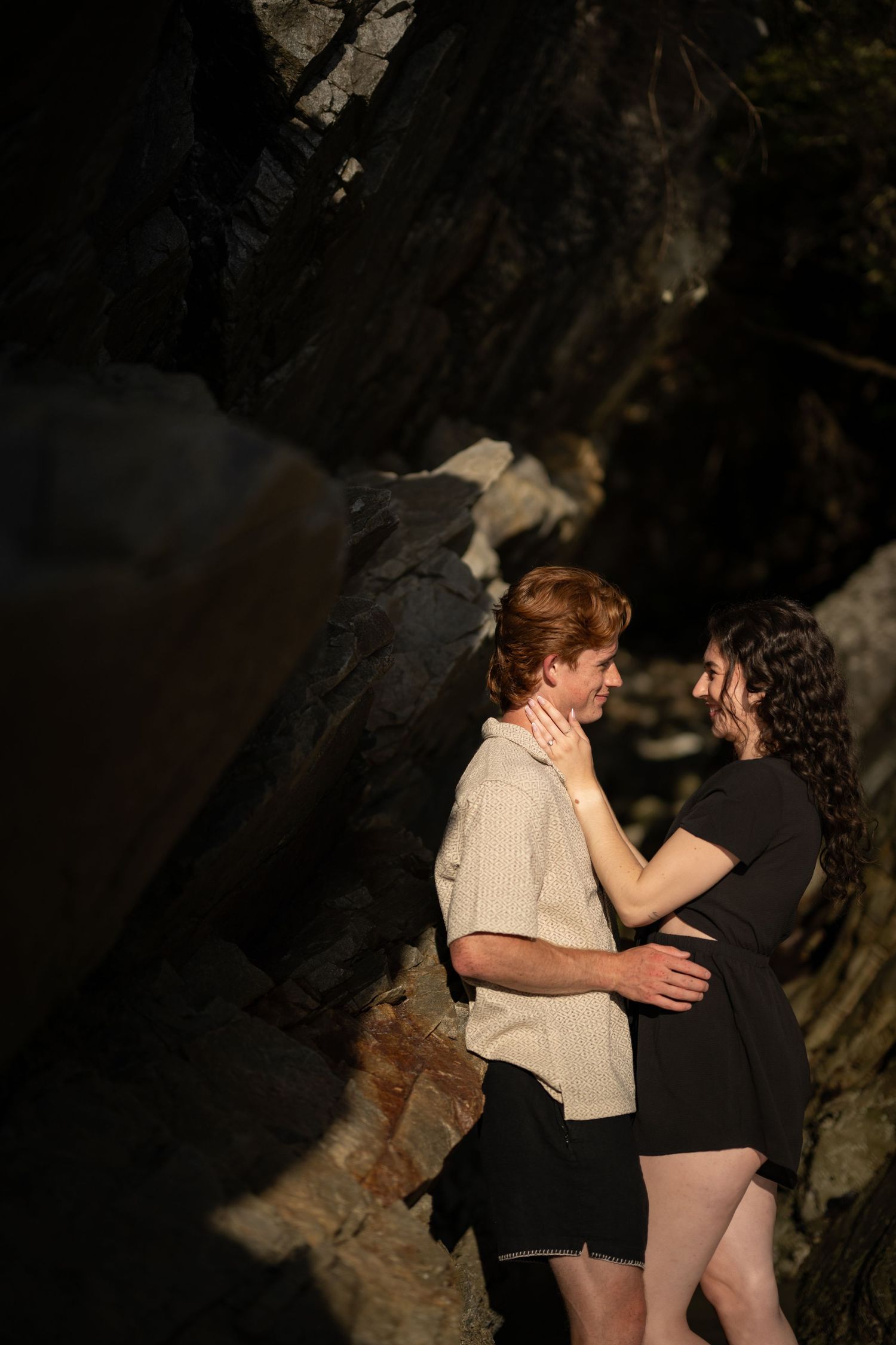 Romantic moment captured against dark rocky cliffs near the ocean.