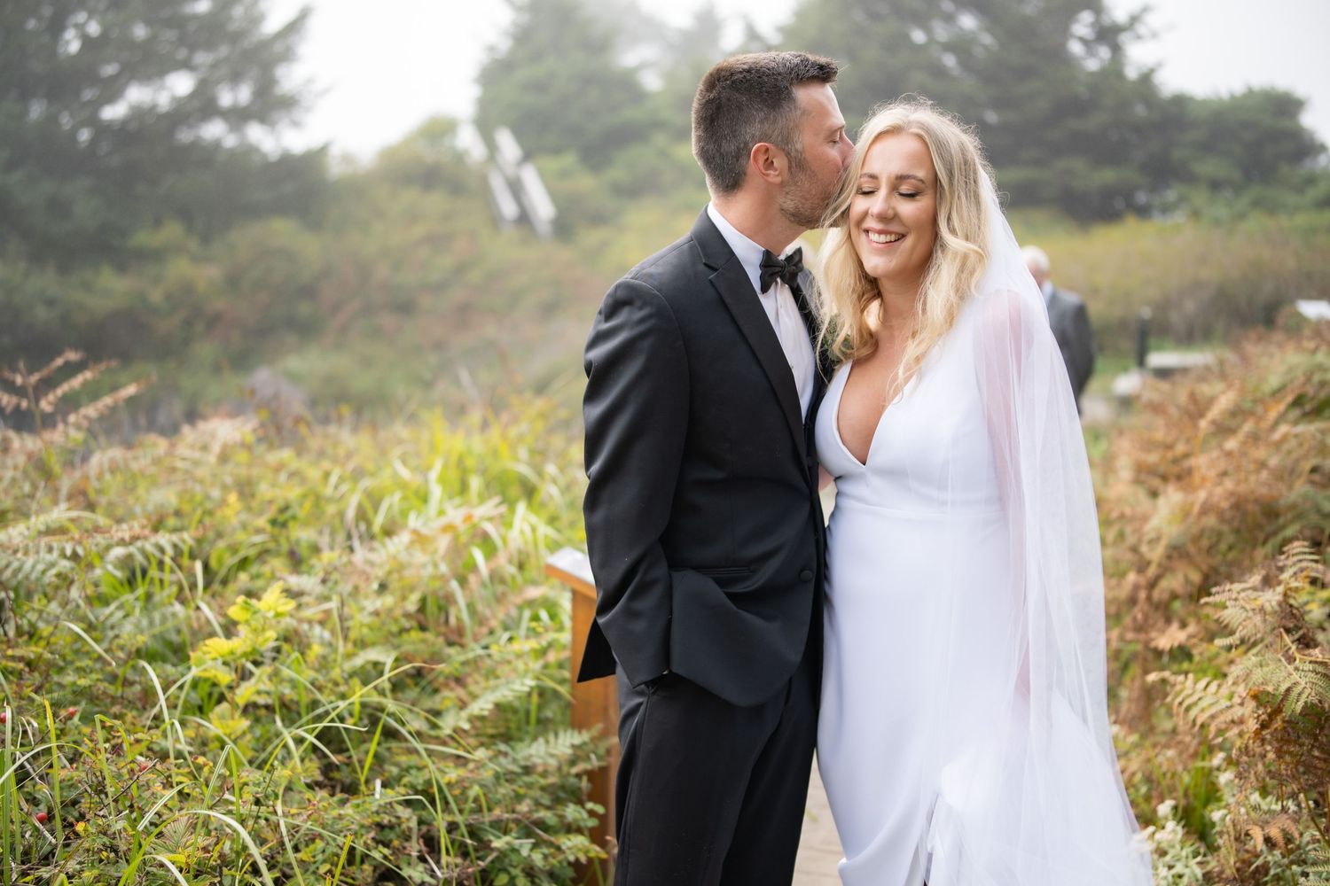Newlyweds share intimate moments on nature trail surrounded by greenery.