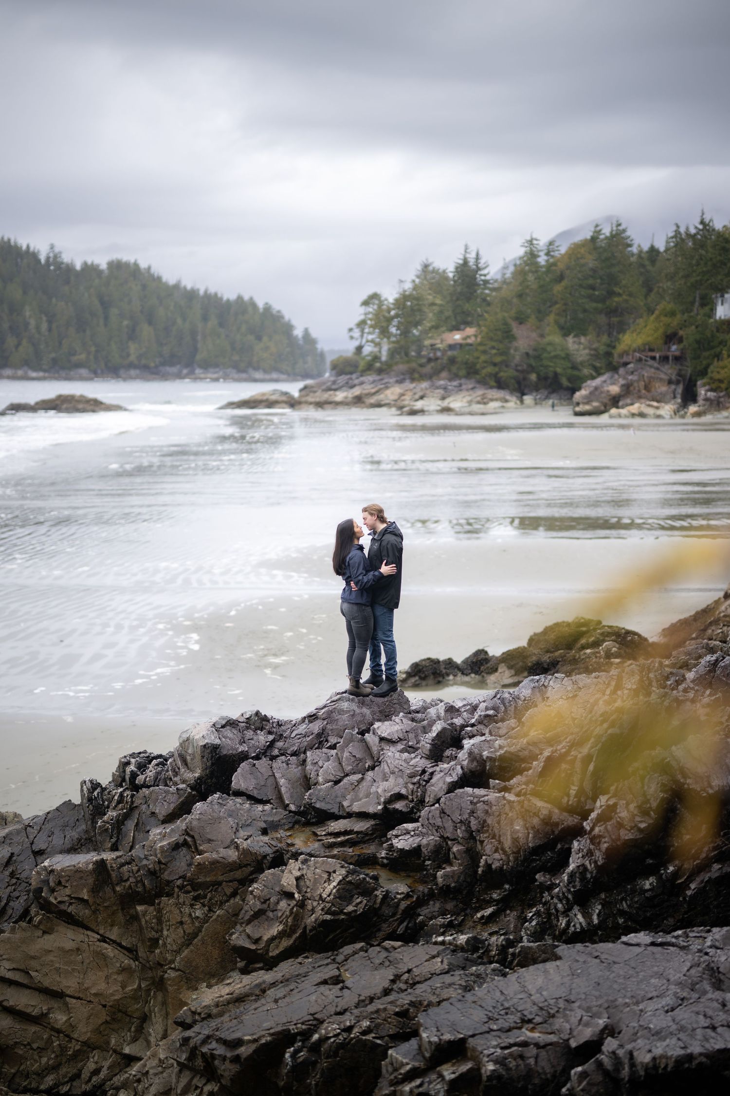 A couple embracing on rocky coastal cliffs overlooking a moody ocean landscape.