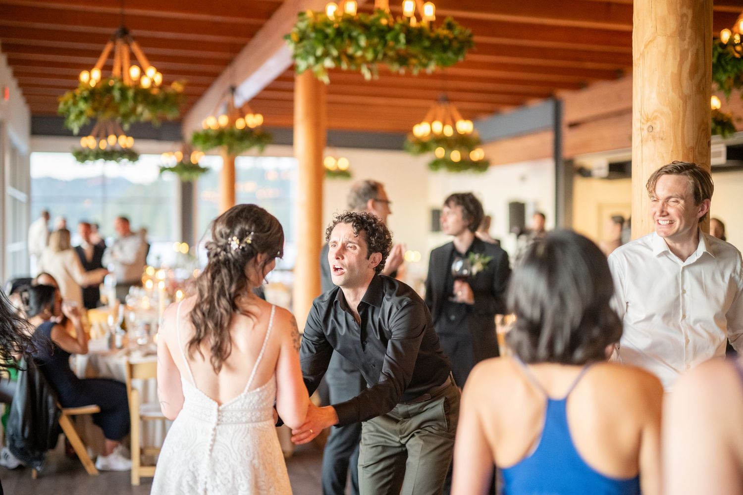 Wedding reception venue with exposed wooden beams and decorative lighting during dance celebrations.