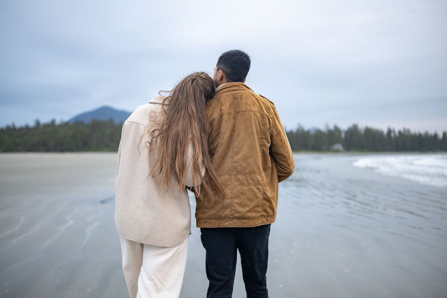 Two people walking together along a misty beach shoreline.