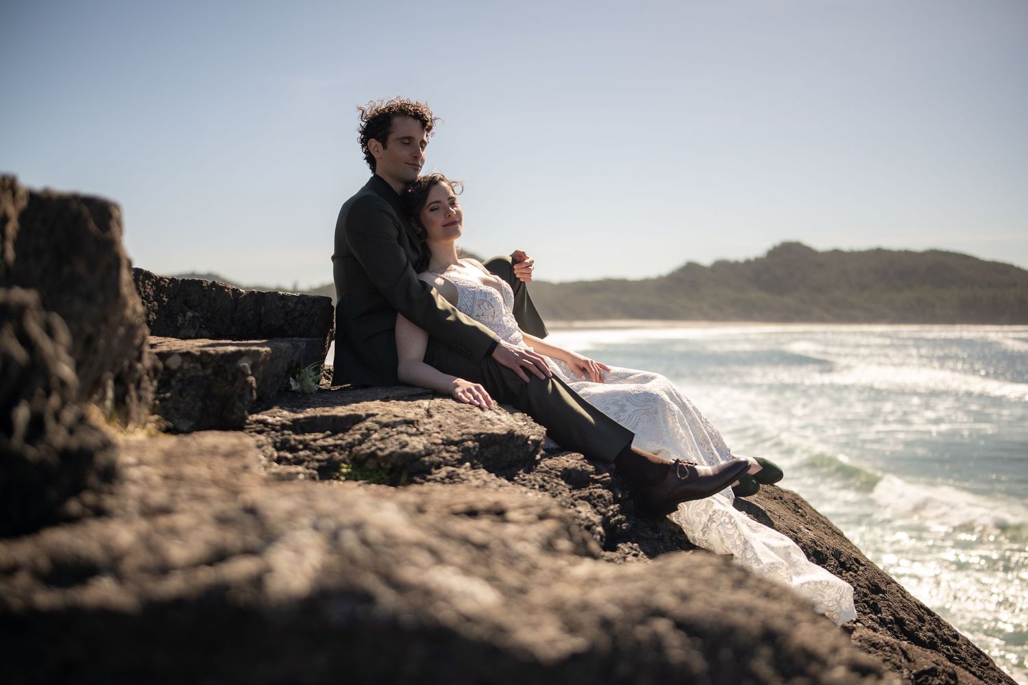 Couple relaxing on rocky coastal cliffs with dramatic ocean views.