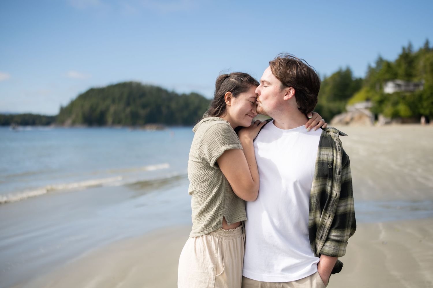 A tender moment shared between two people on a sunny beach with coastal views.