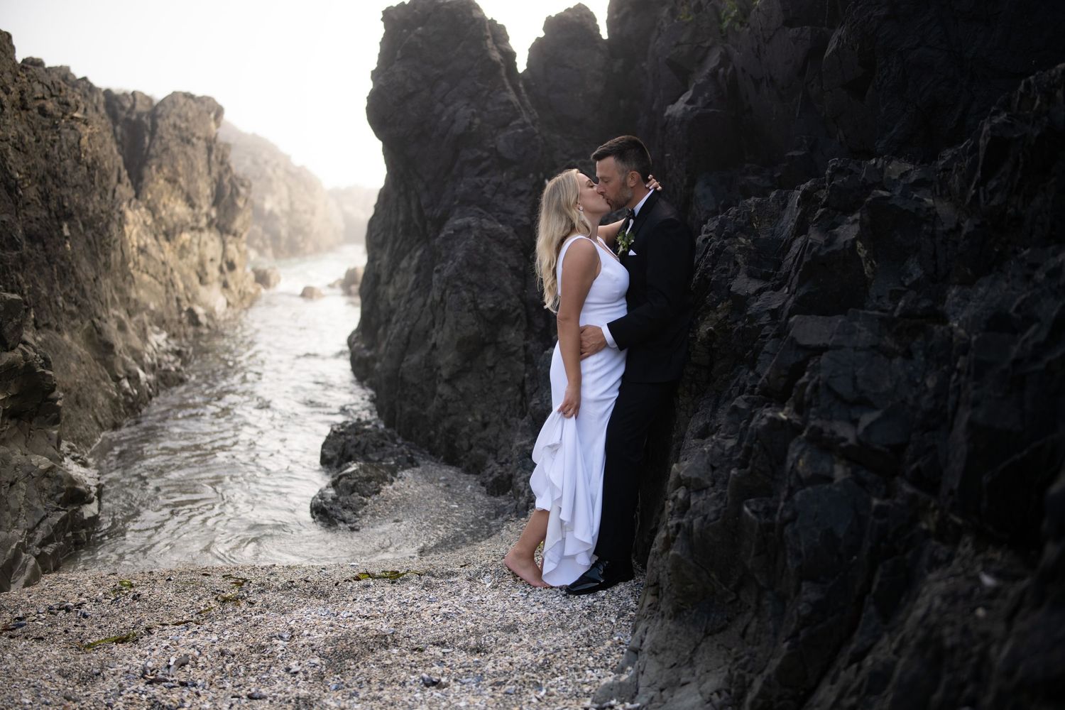 Wedding couple explores dramatic rocky cove with towering cliffs.