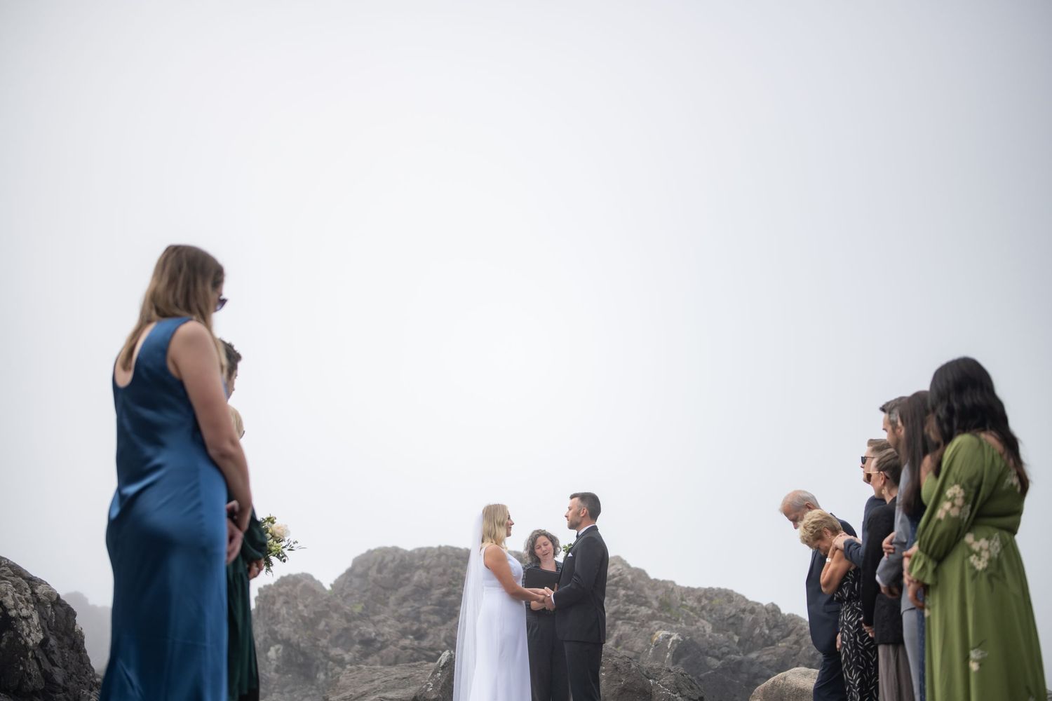 Wedding ceremony takes place on a foggy beach with rocky cliffs in the background.