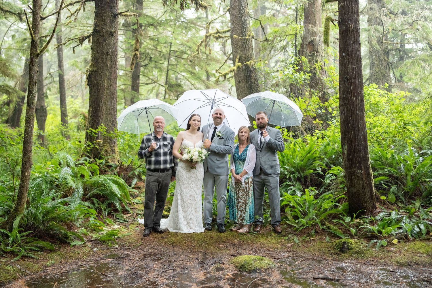 Wedding attendees gather on a forest path surrounded by lush greenery.