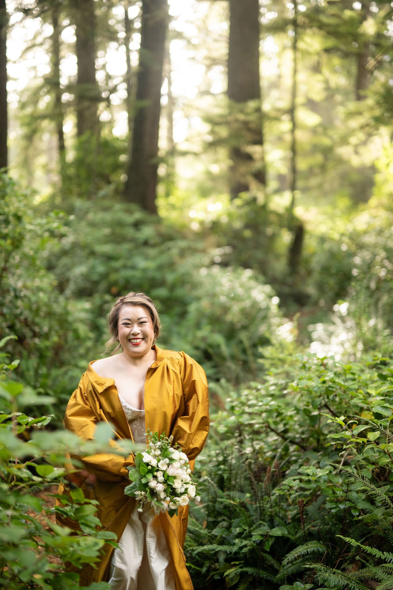 A bright yellow dress stands out against the lush green forest backdrop while holding a white floral bouquet.