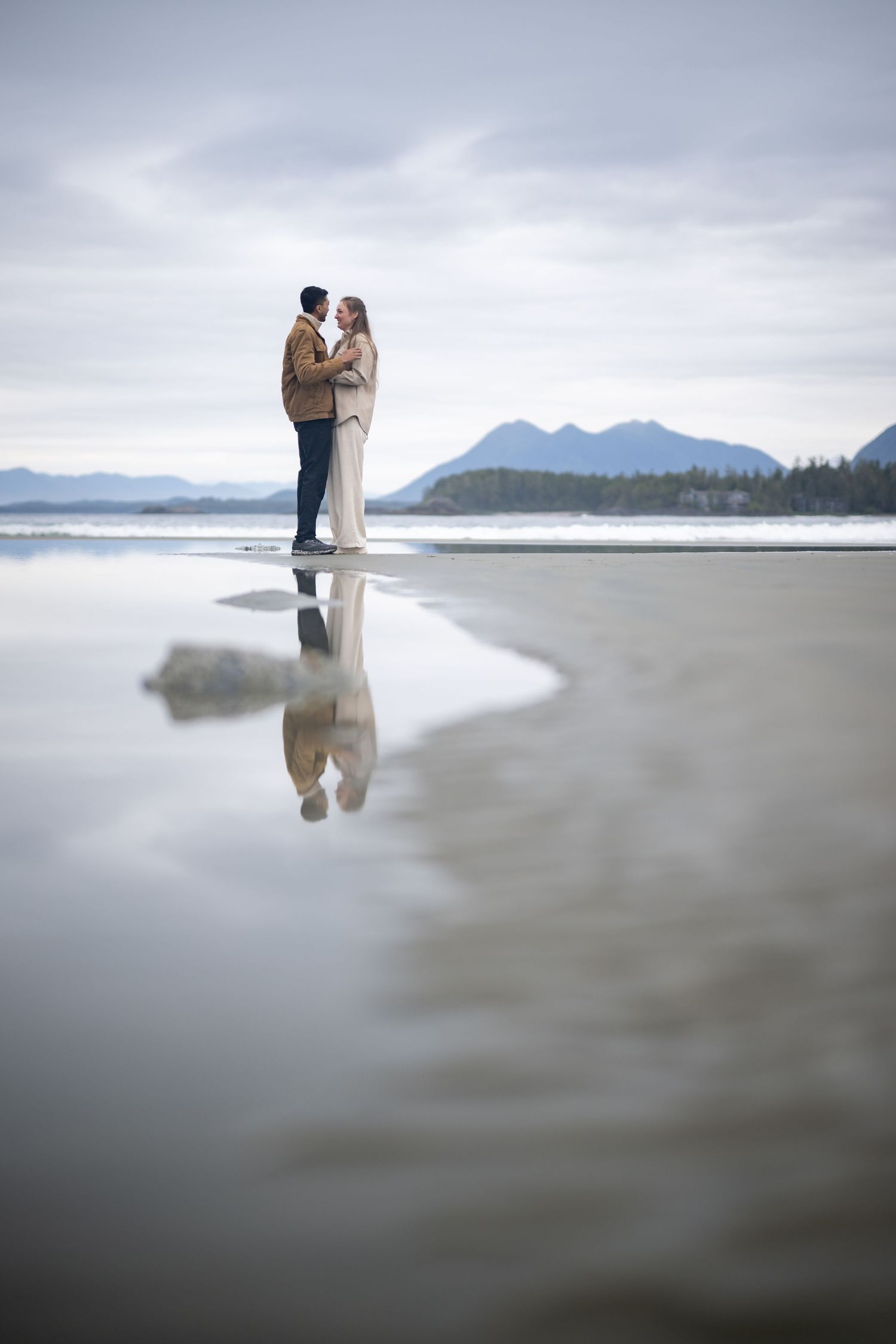 Dreamy beach portraits with reflections in wet sand and mountain backdrop.
