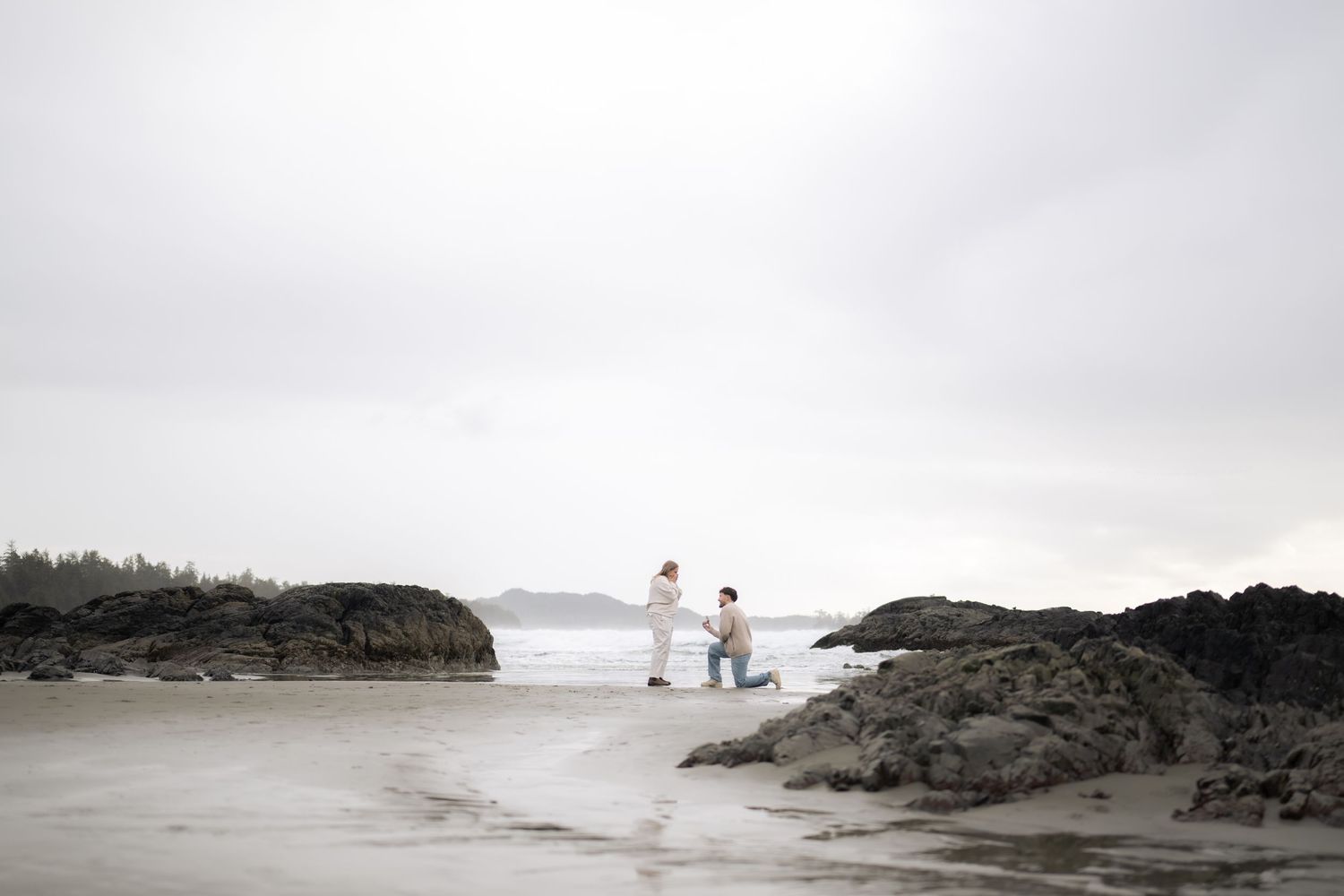 Couple walking along a misty rocky beach coastline with dramatic overcast sky.