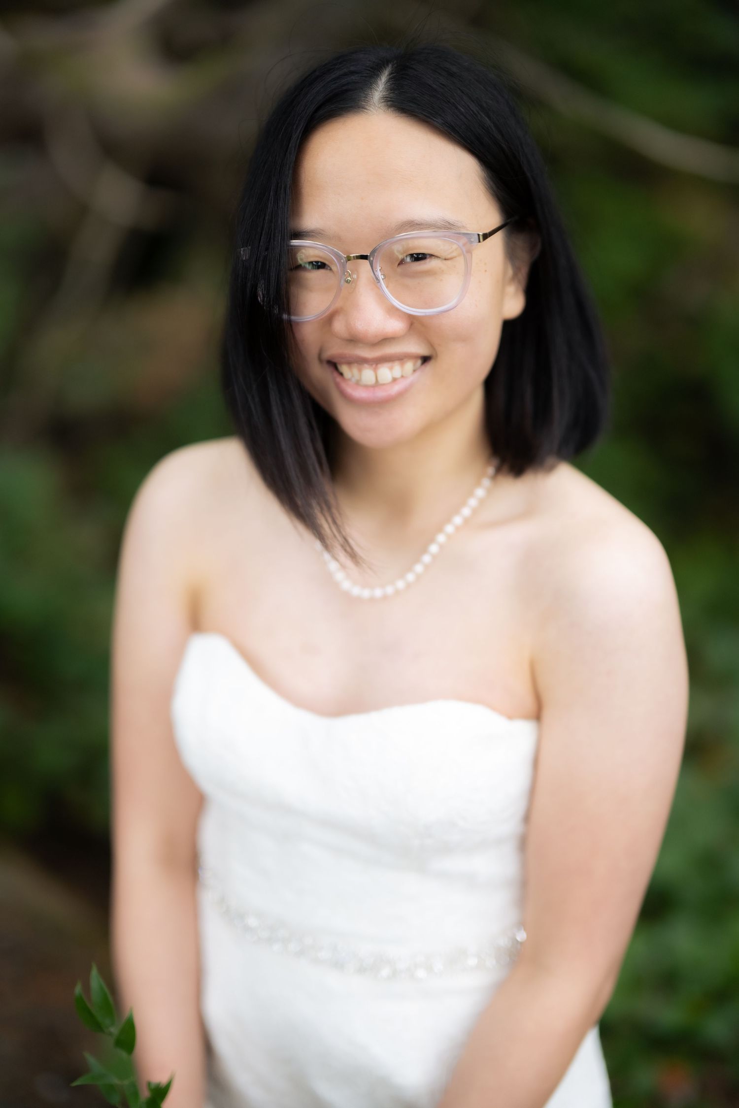 A person in a white wedding dress with a pearl necklace smiles warmly.