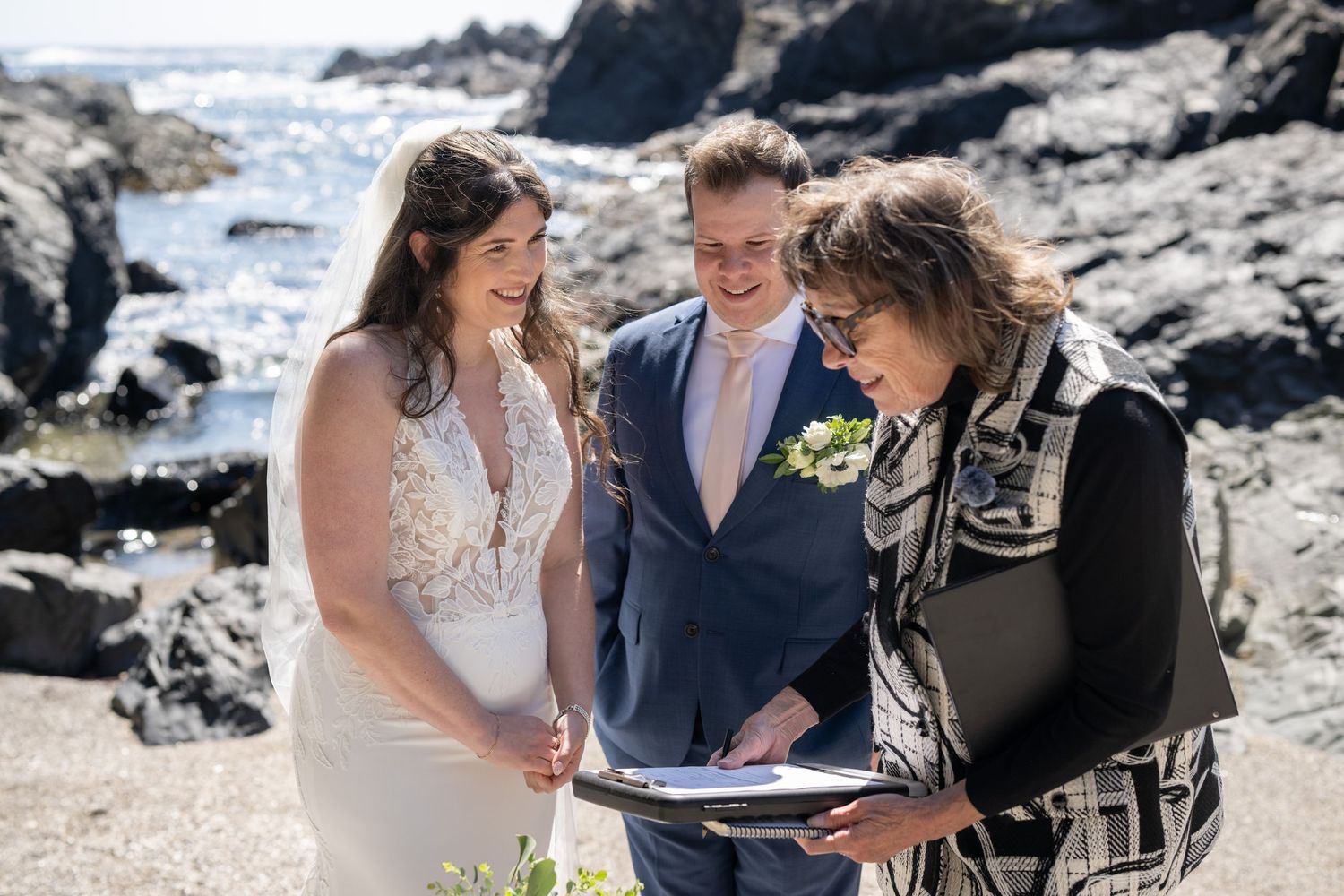 Small wedding gathering on a scenic beach with rocky cliffs.