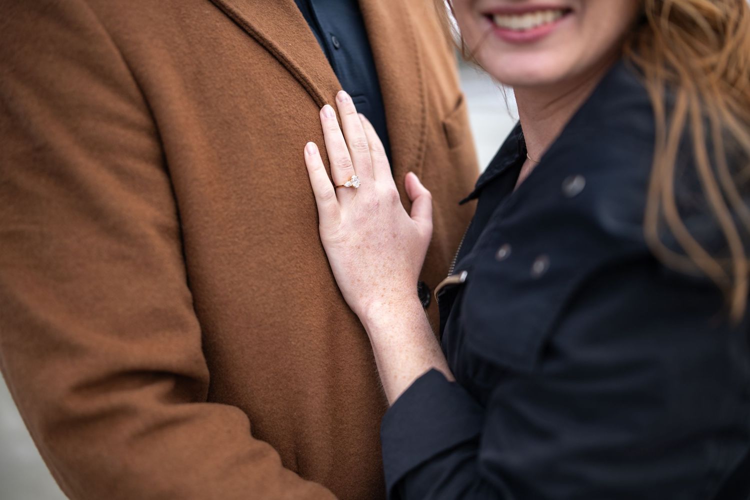 A close-up shot shows hands embracing against brown and black coats during an intimate moment.