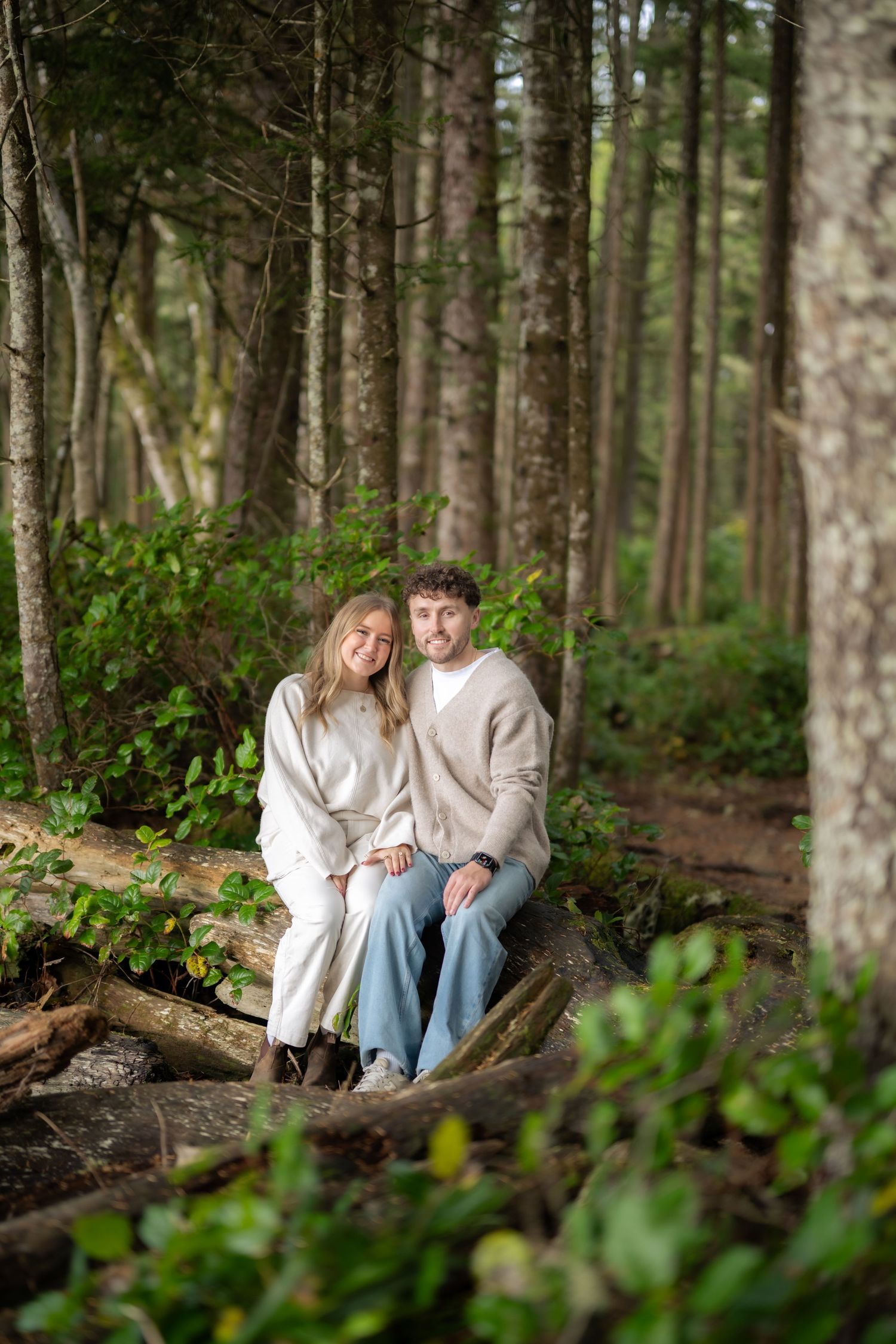 Couple sitting on fallen log in peaceful forest setting wearing light colored clothing.