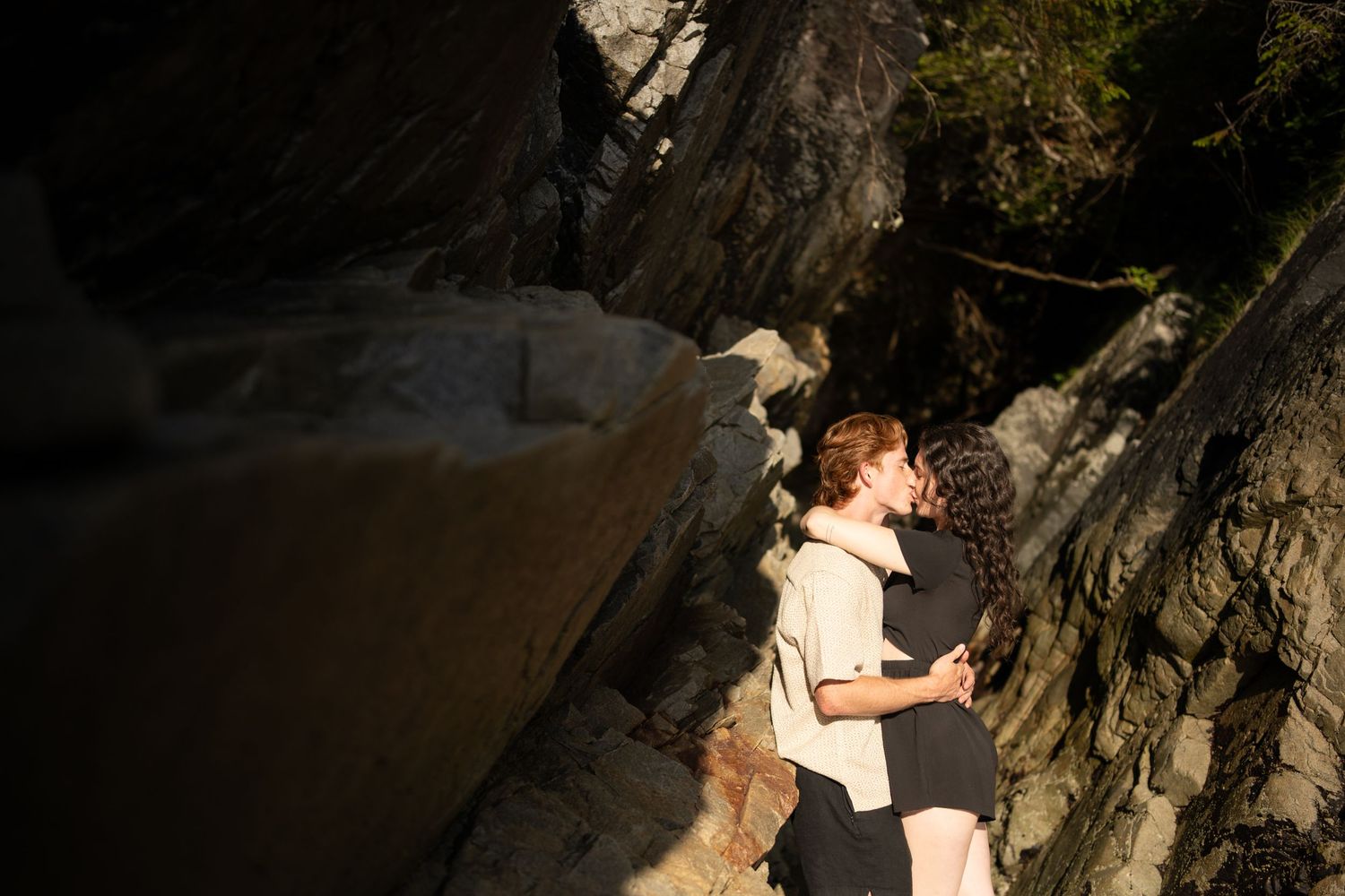 Couple sharing tender moment against natural rock formations by the sea.
