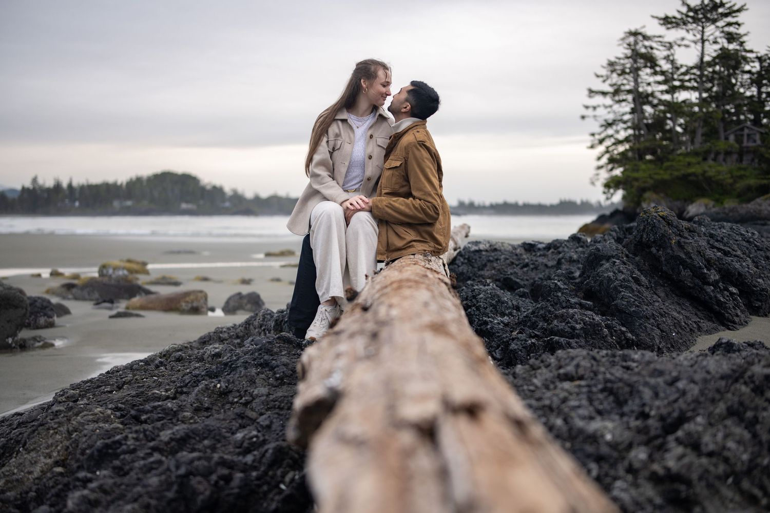 Couple embracing on dramatic black rocks overlooking the Pacific ocean.