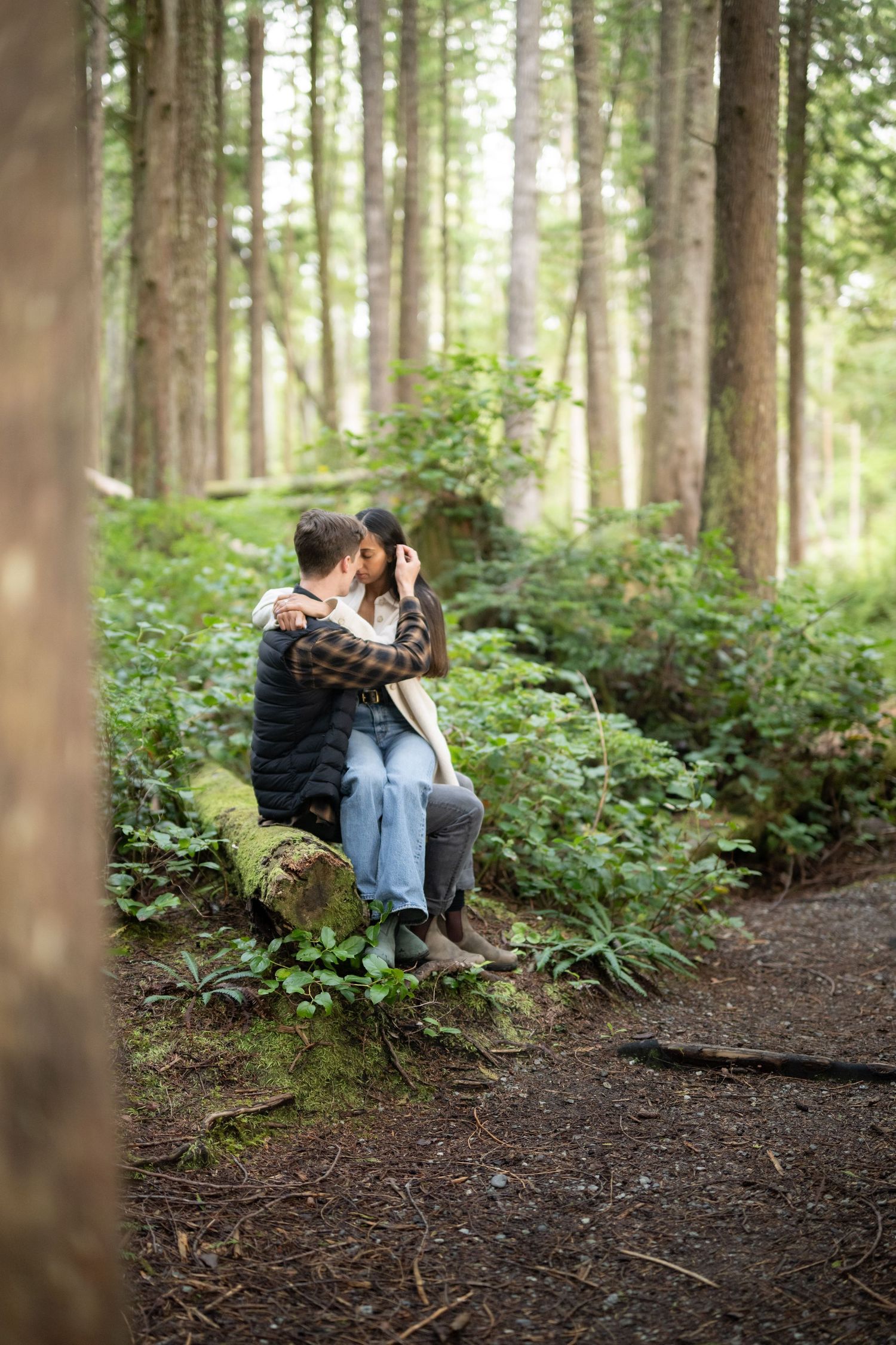 Couple sharing tender moments while seated on a fallen tree in a serene forest setting.