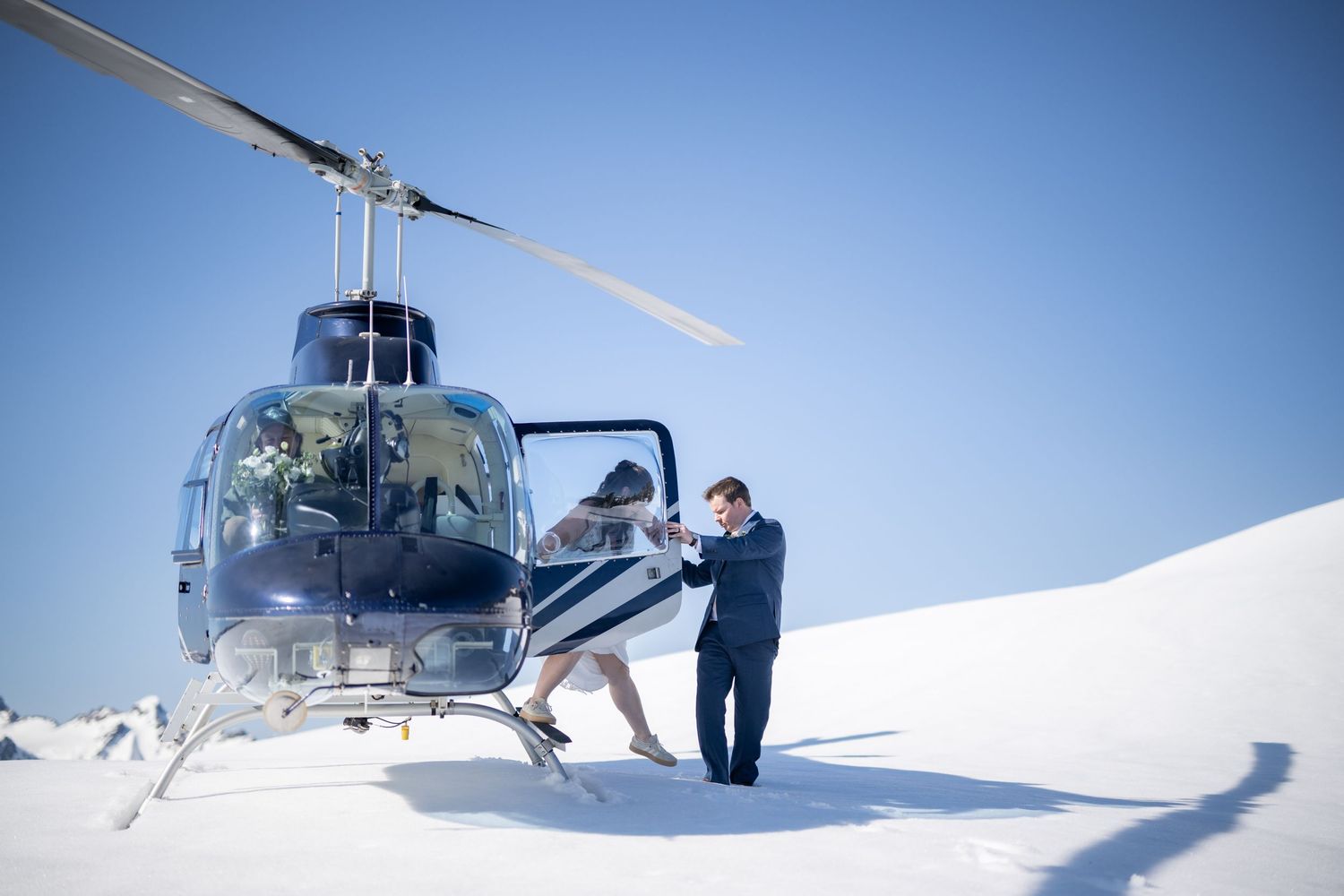 Helicopter landed on snowy mountain peak with passengers disembarking.