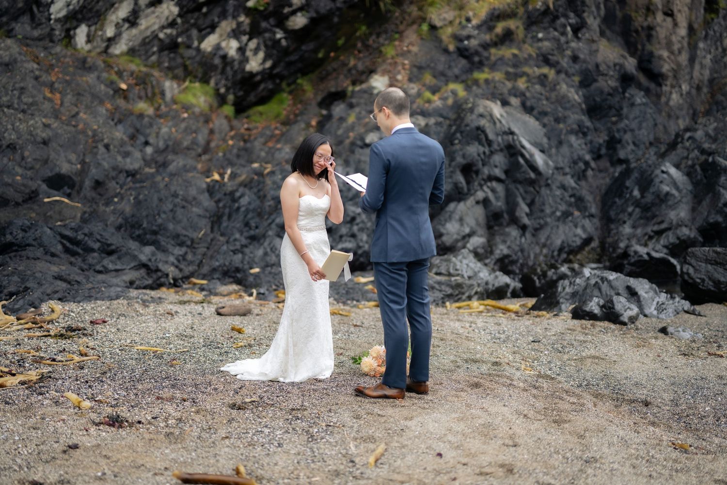 Wedding ceremony unfolds on a scenic beach surrounded by dramatic rock formations.