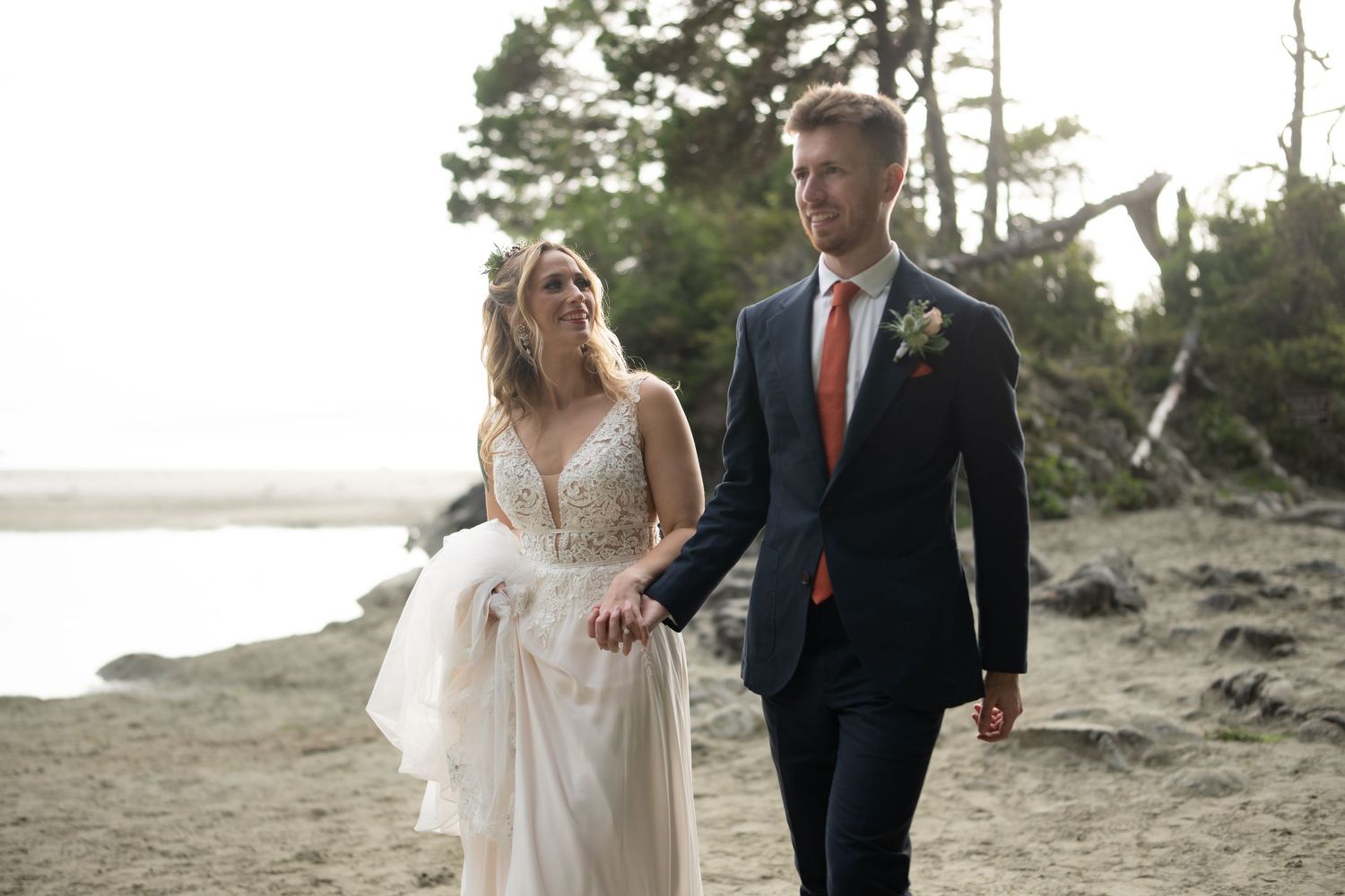 Couple walks along scenic coastal path during sunset wedding photoshoot.
