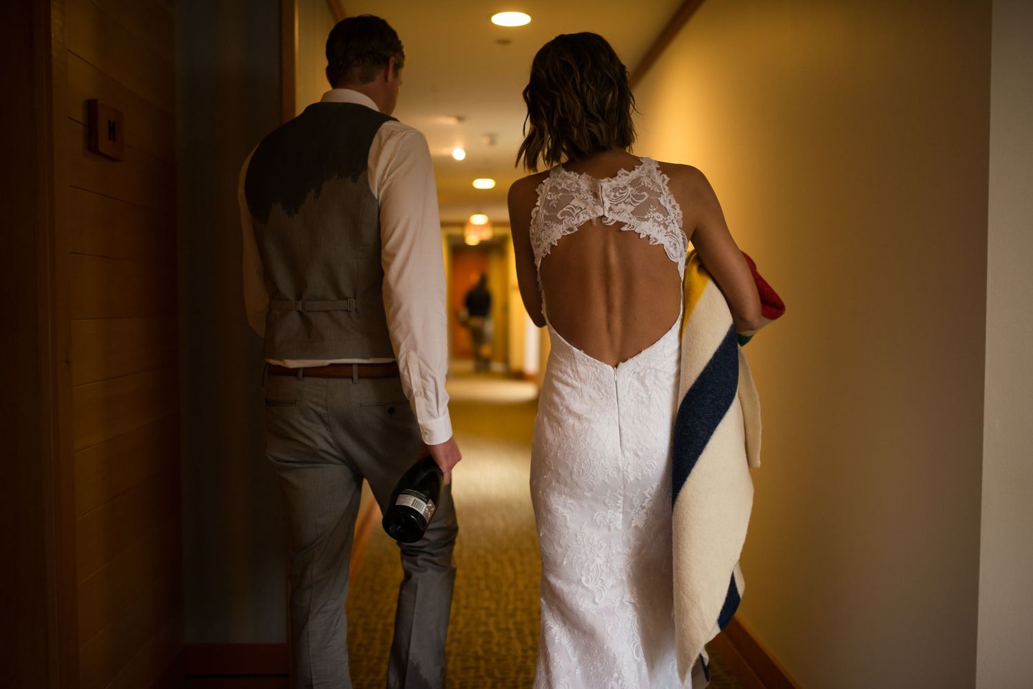A couple walks down a hotel corridor wearing wedding attire.
