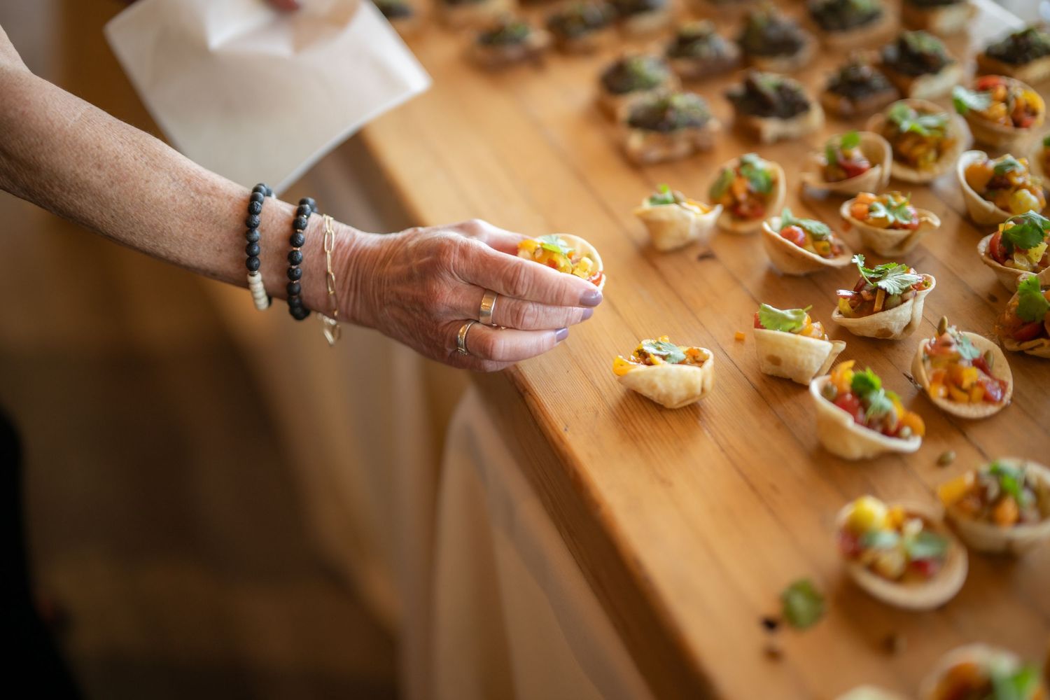 Close-up of hand reaching for appetizers arranged on wooden serving board.