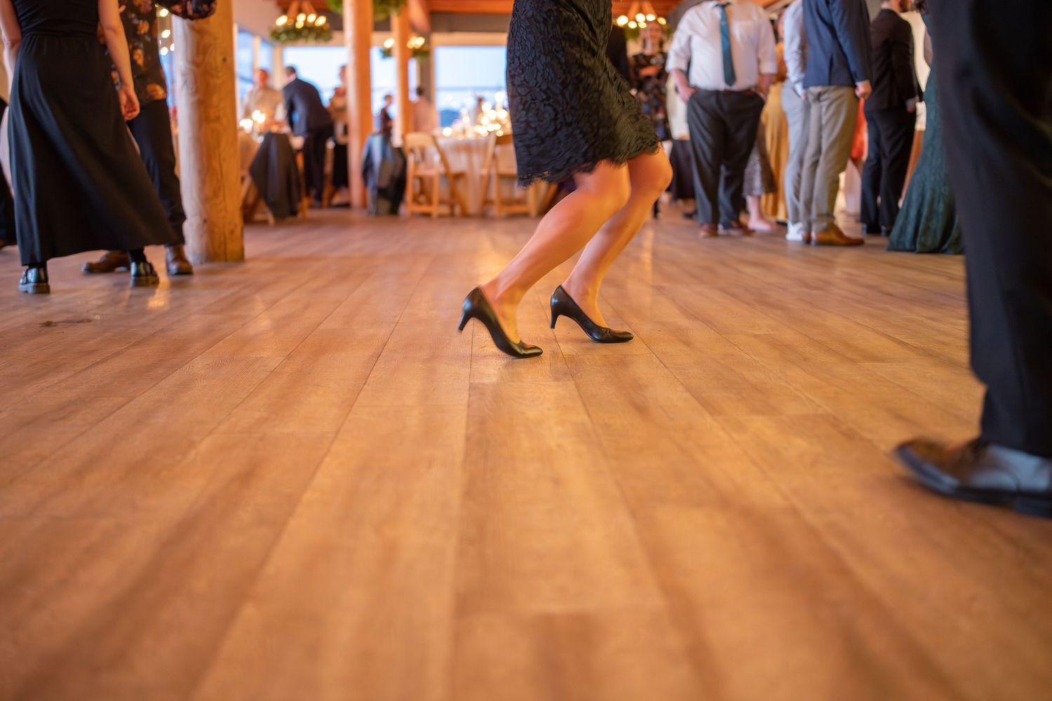 Close-up view of dancing feet on a polished wooden floor at a wedding reception.