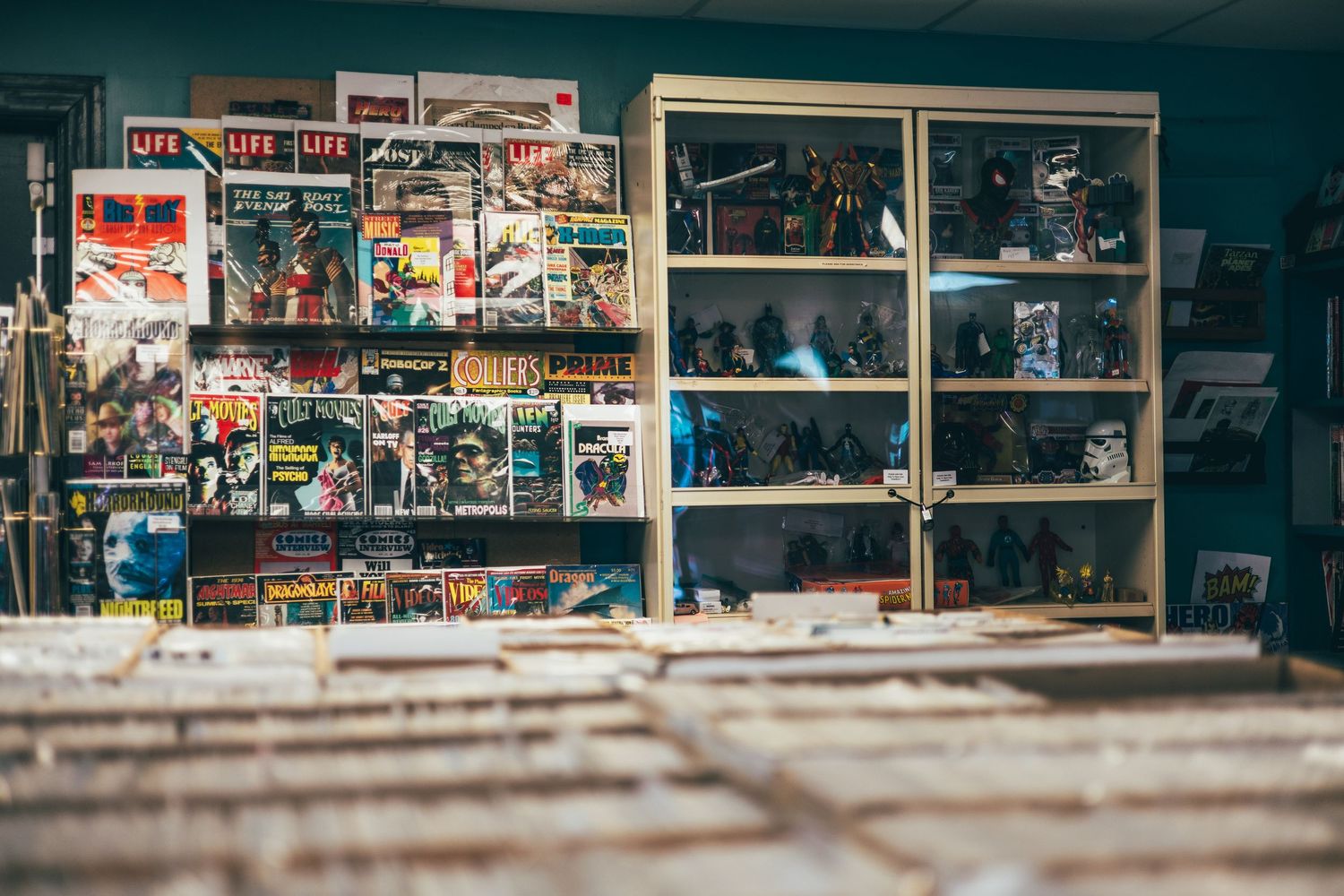 Vintage comic books and collectible figurines displayed on shelves beside crates of records in a cozy comic and collectibles shop.