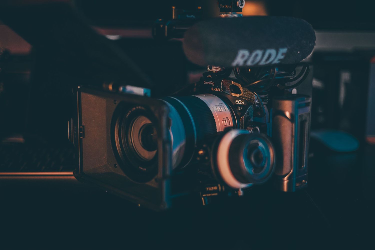 A cinema-style video camera rig with a Rode microphone and matte box glows in moody, low-light studio lighting.
