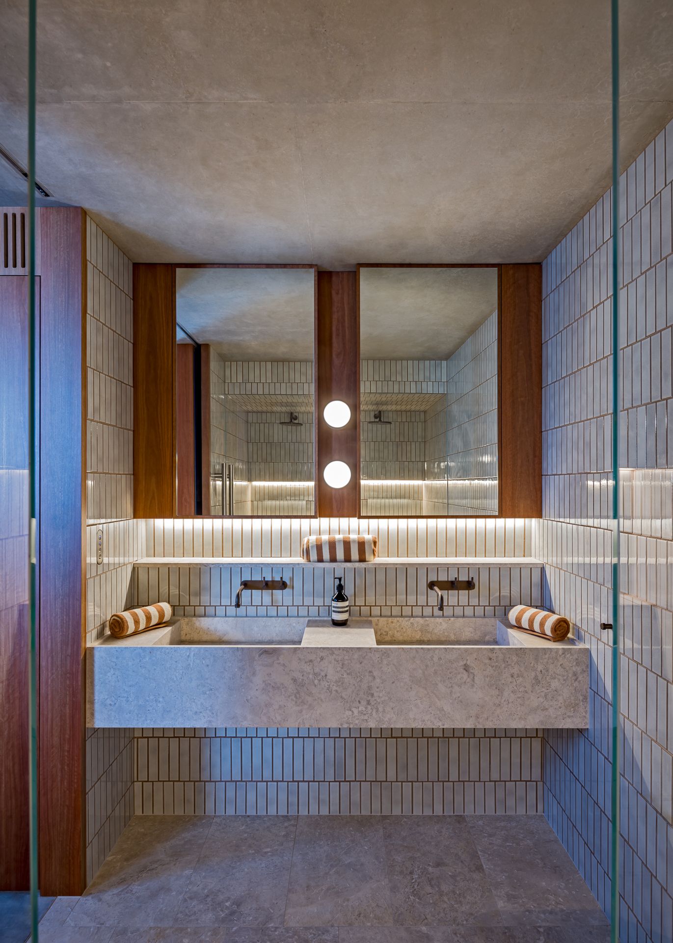 Contemporary bathroom featuring a double stone vanity, mirrors framed in timber, globe lights, and a glass shower screen.