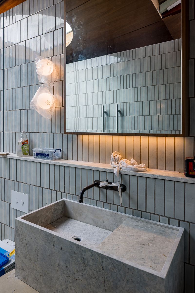Modern bathroom with a rectangular concrete sink, matte black wall-mounted faucet, sage green vertical tiles, and a mirrored cabinet with wa