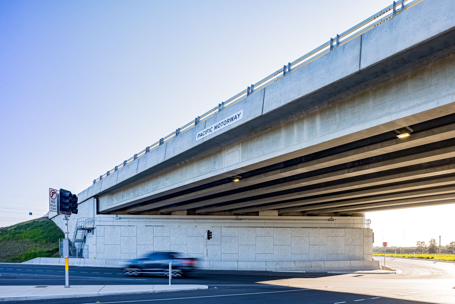 Motorway overpass with concrete abutment and traffic lights as a car passes underneath at dusk.