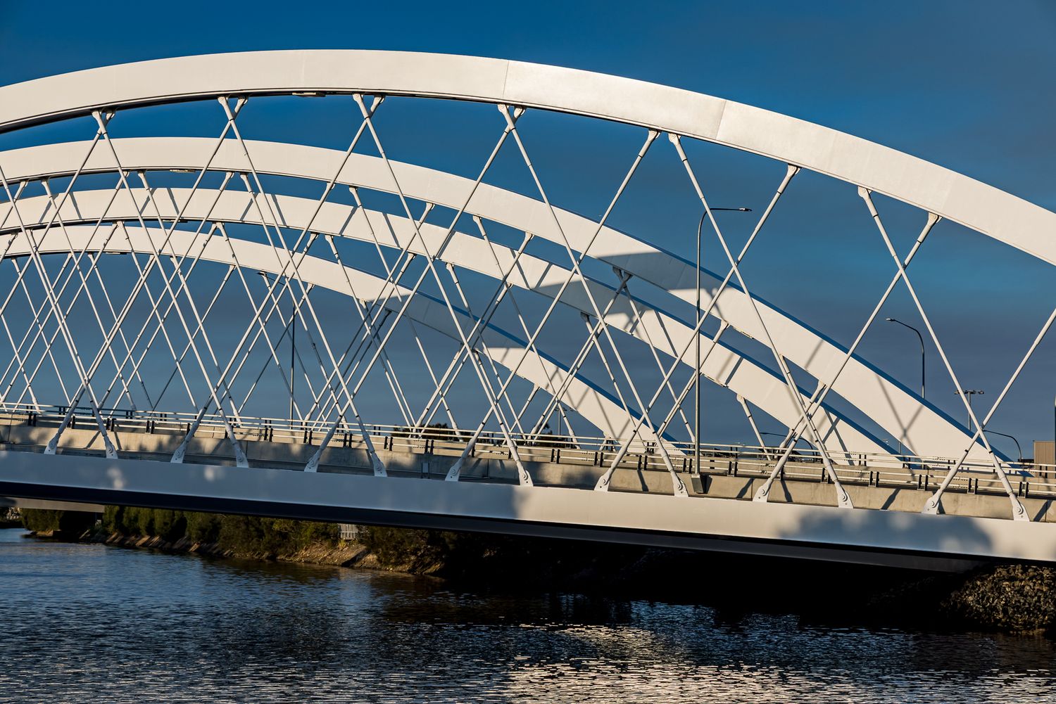 Close-up of white steel arches and diagonal cable supports on a bridge above rippling river water.