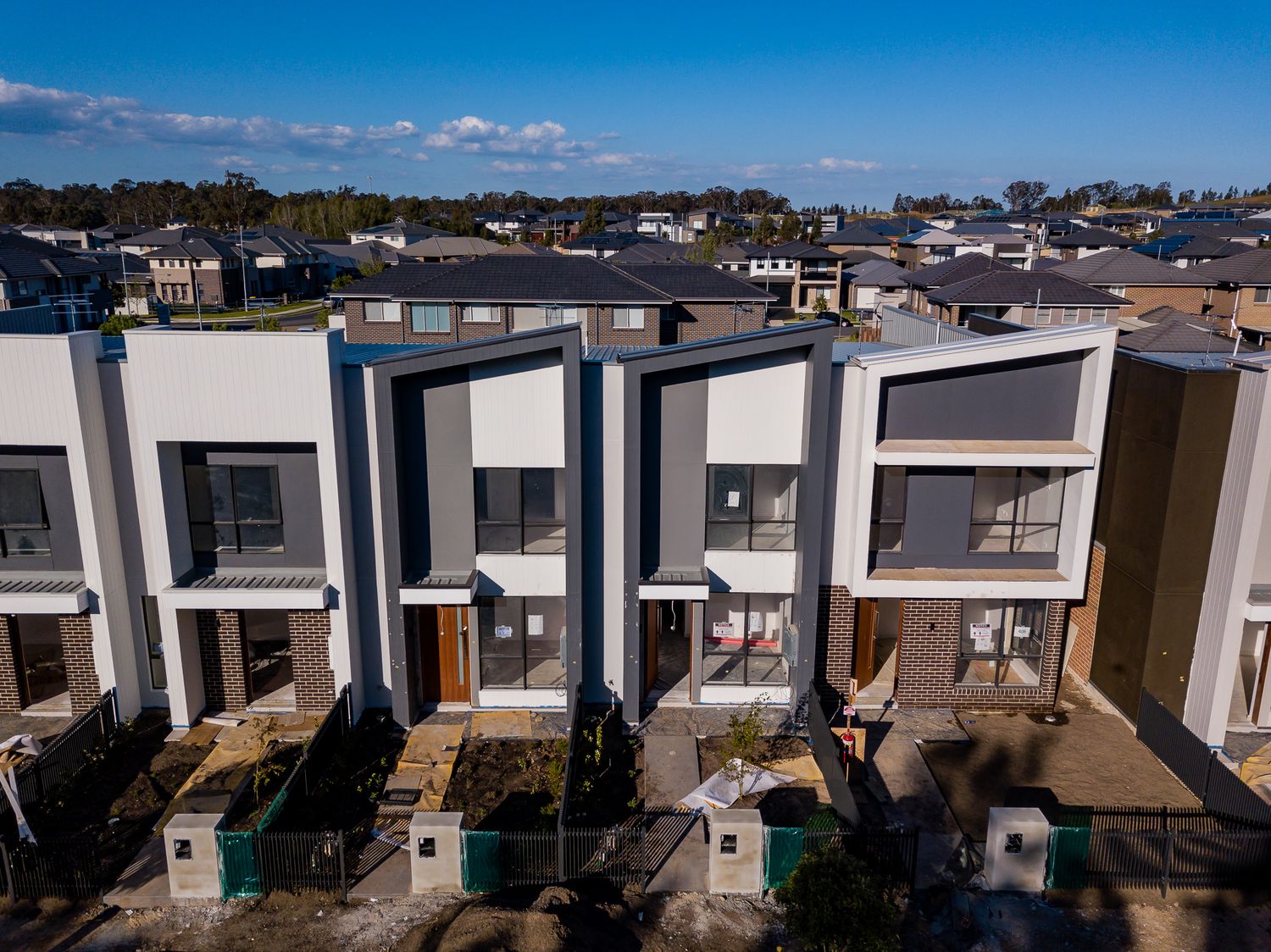 Modern townhouses with contemporary grey and white facades, small front gardens and a suburban estate stretching behind them.