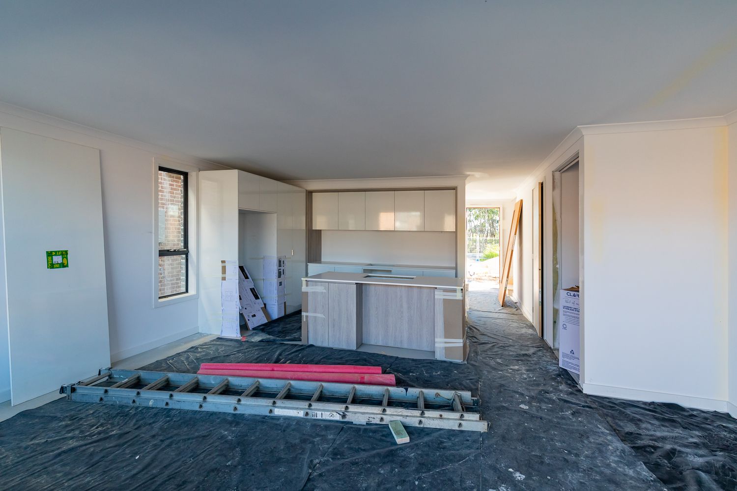 Open-plan interior of a new home under construction featuring a kitchen island, cabinetry and protective plastic floor sheeting.