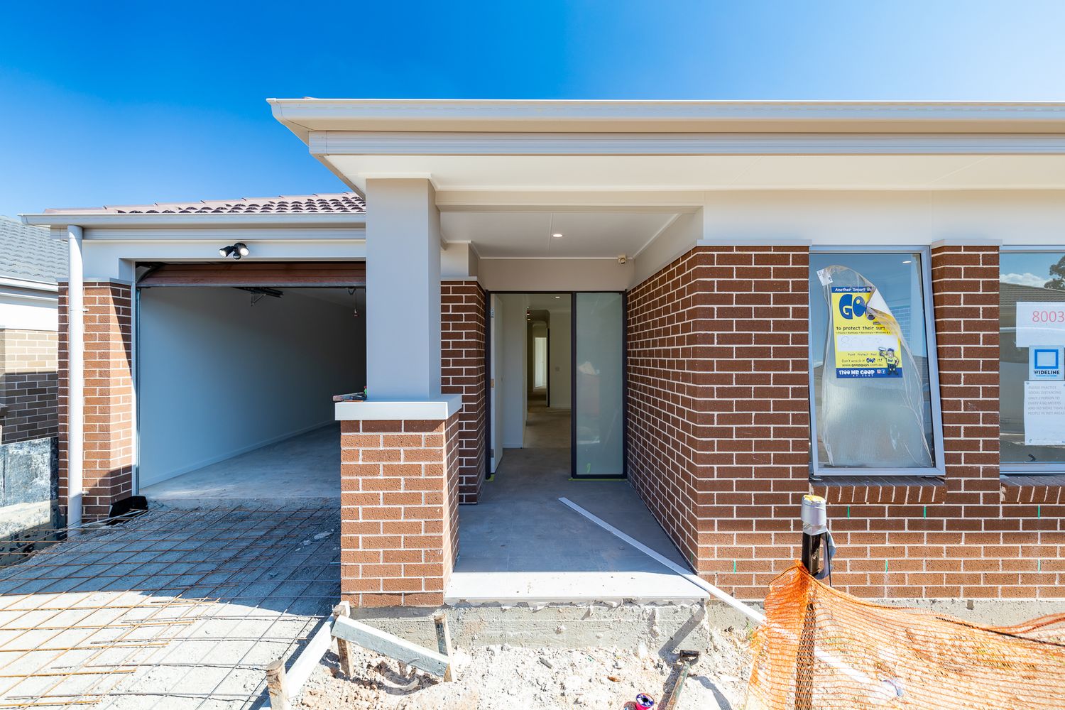 Front entrance of a new brick home under construction with a covered porch, garage and a for sale sign in the window.