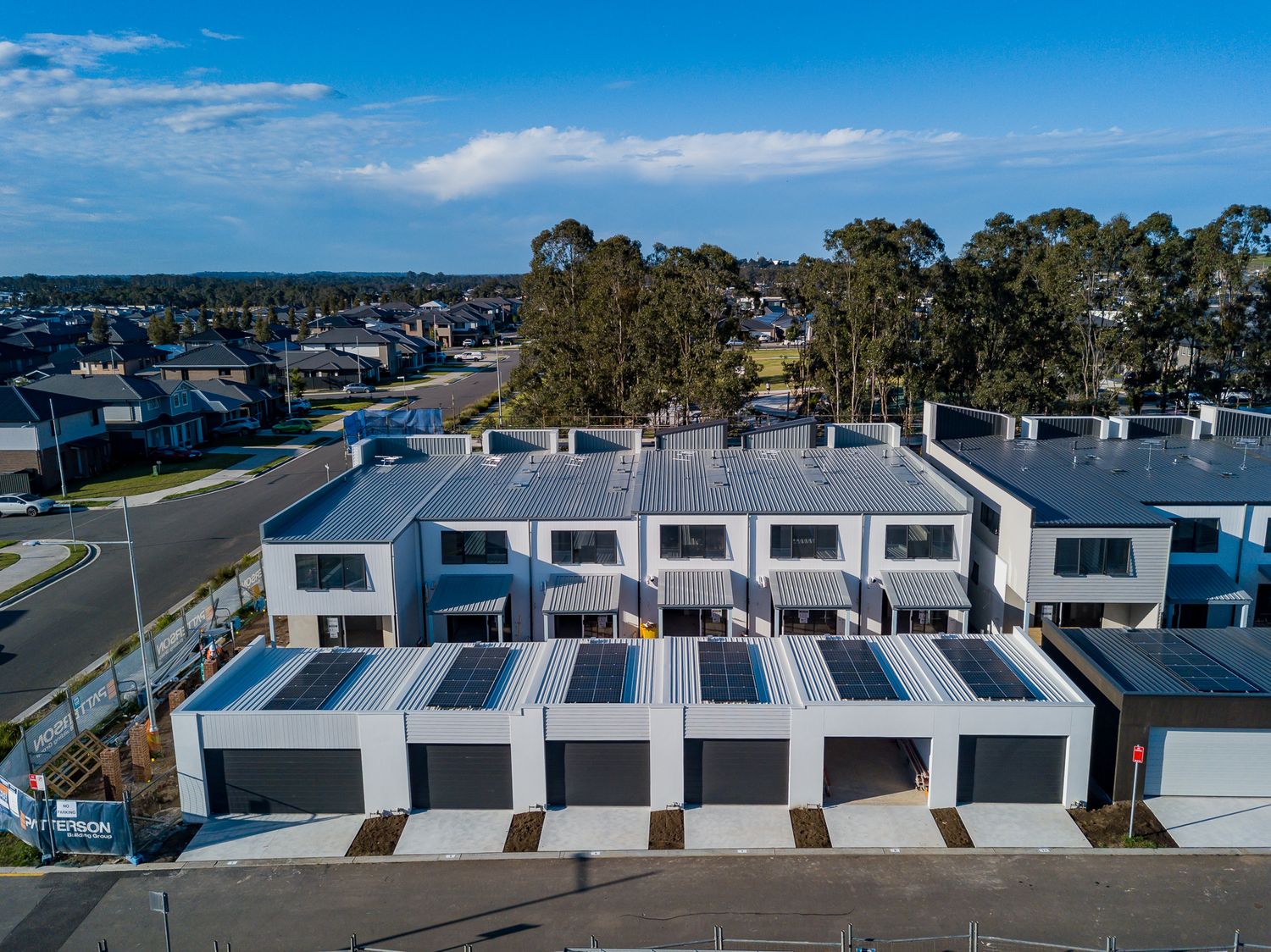 Aerial view of a new row of modern two-storey townhouses with garages and solar panels in a suburban housing estate.