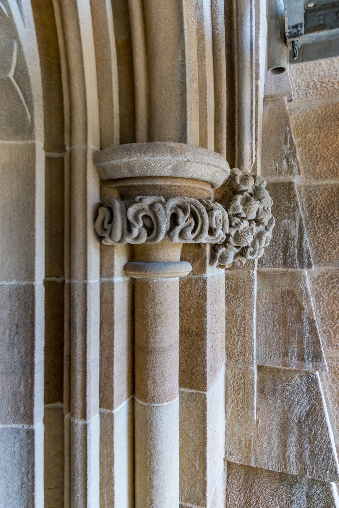 Sandstone column with a carved scroll capital and floral corbel set against a dressed stone wall.
