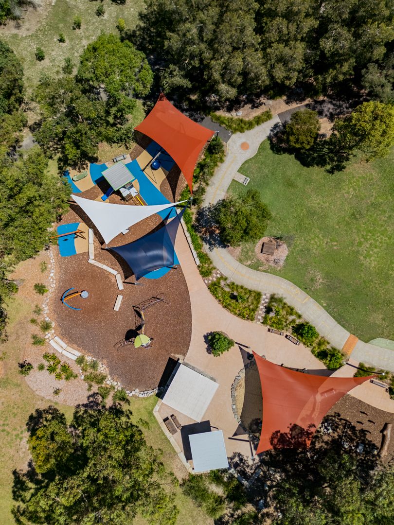Aerial view of a nature play space with colorful shade sails, curving paths and bushland surrounds.