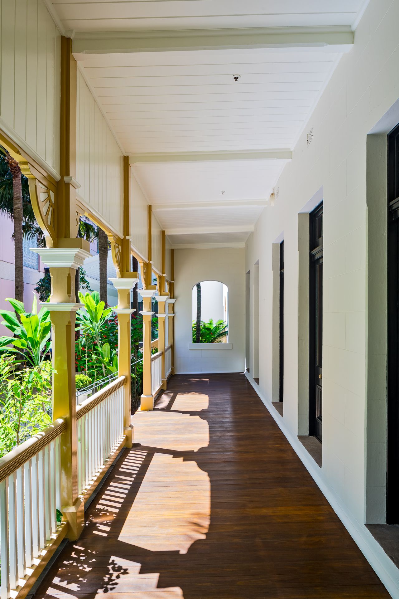Long heritage veranda with polished timber floors, white balustrade and tropical plants casting dappled shadows.
