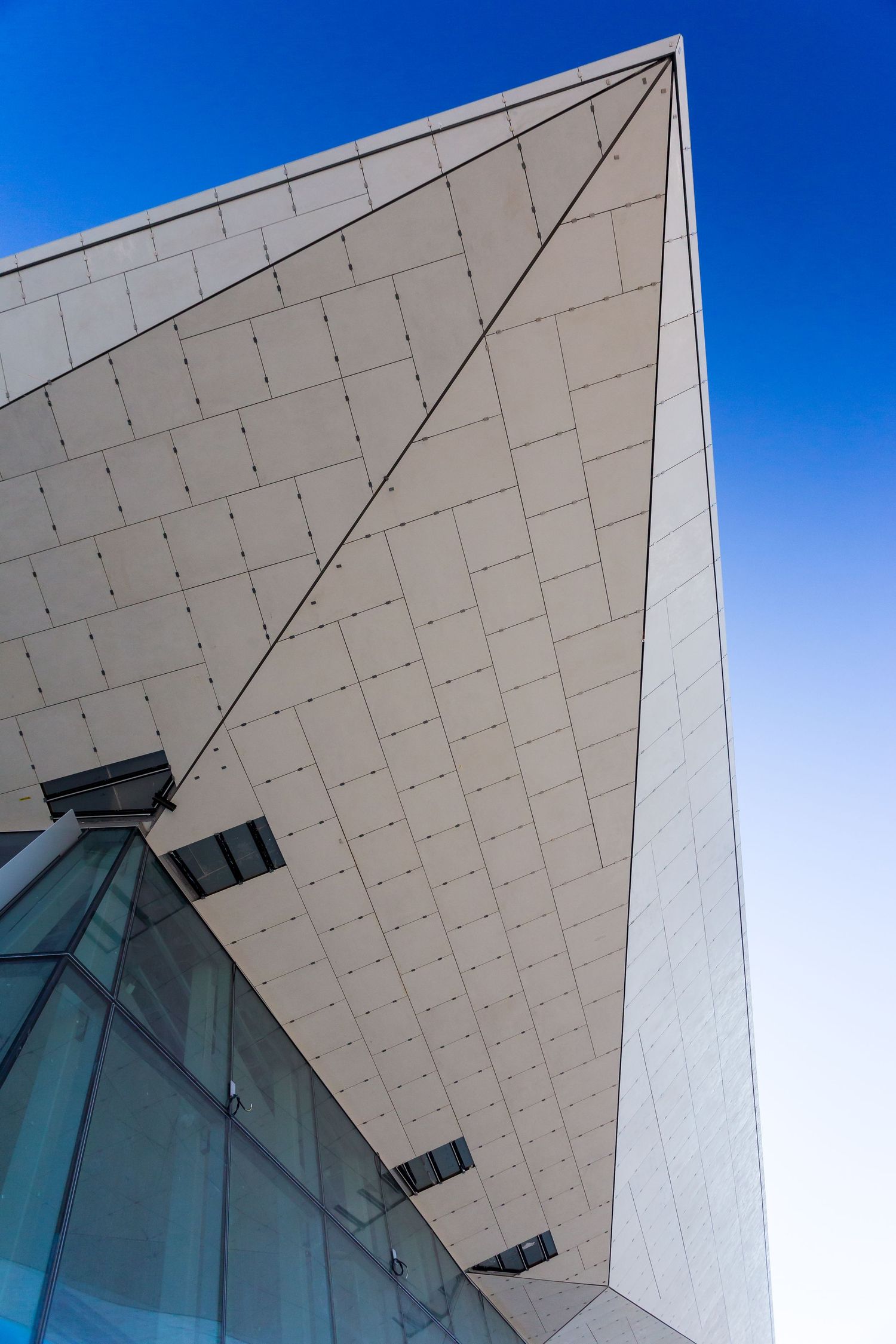 Angular white paneled building facade with glass windows rising against a deep blue sky.